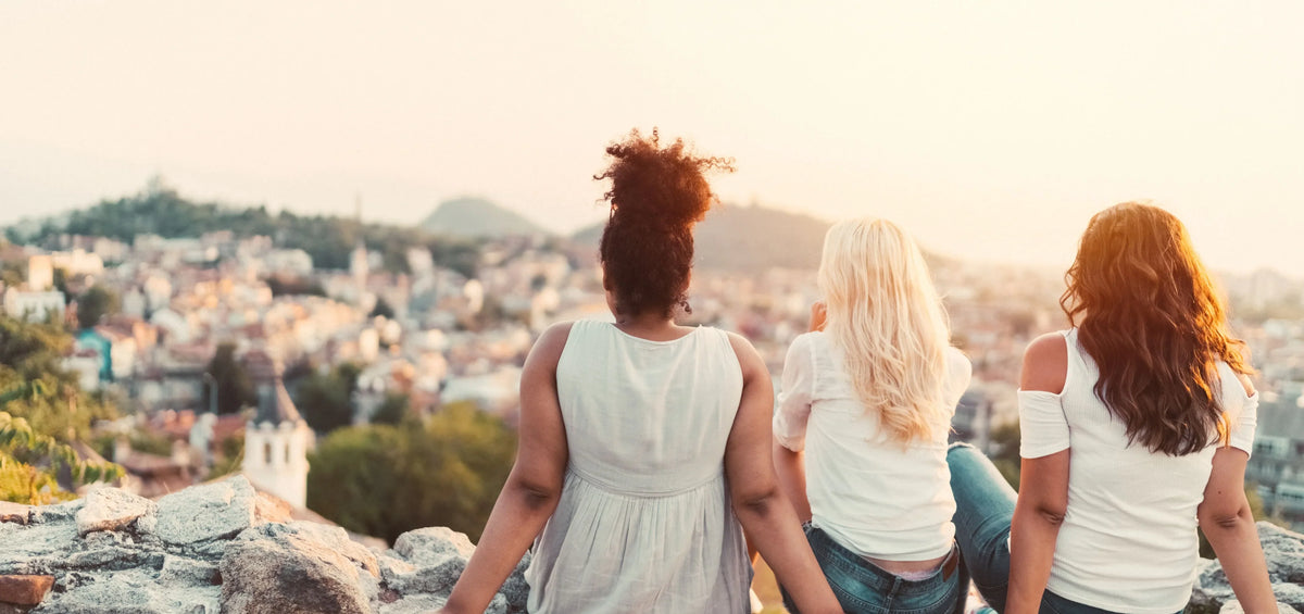 image of women supporting each other while sitting facing away and looking over a cityscape