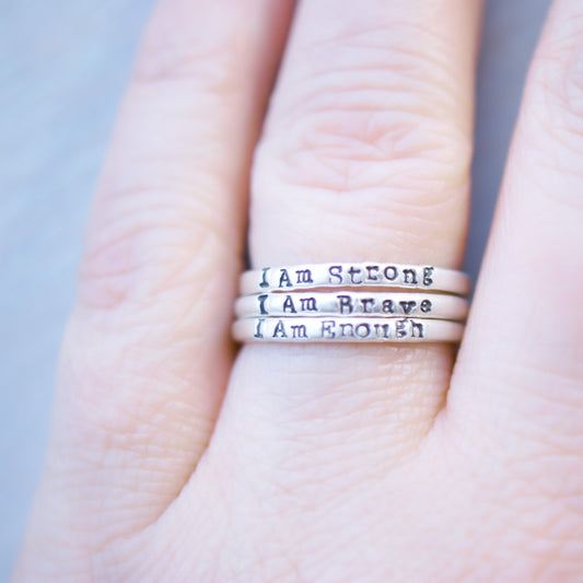 Three rings stacked on hand, each stamped with I Am Enough, I Am Strong, I Am Brave