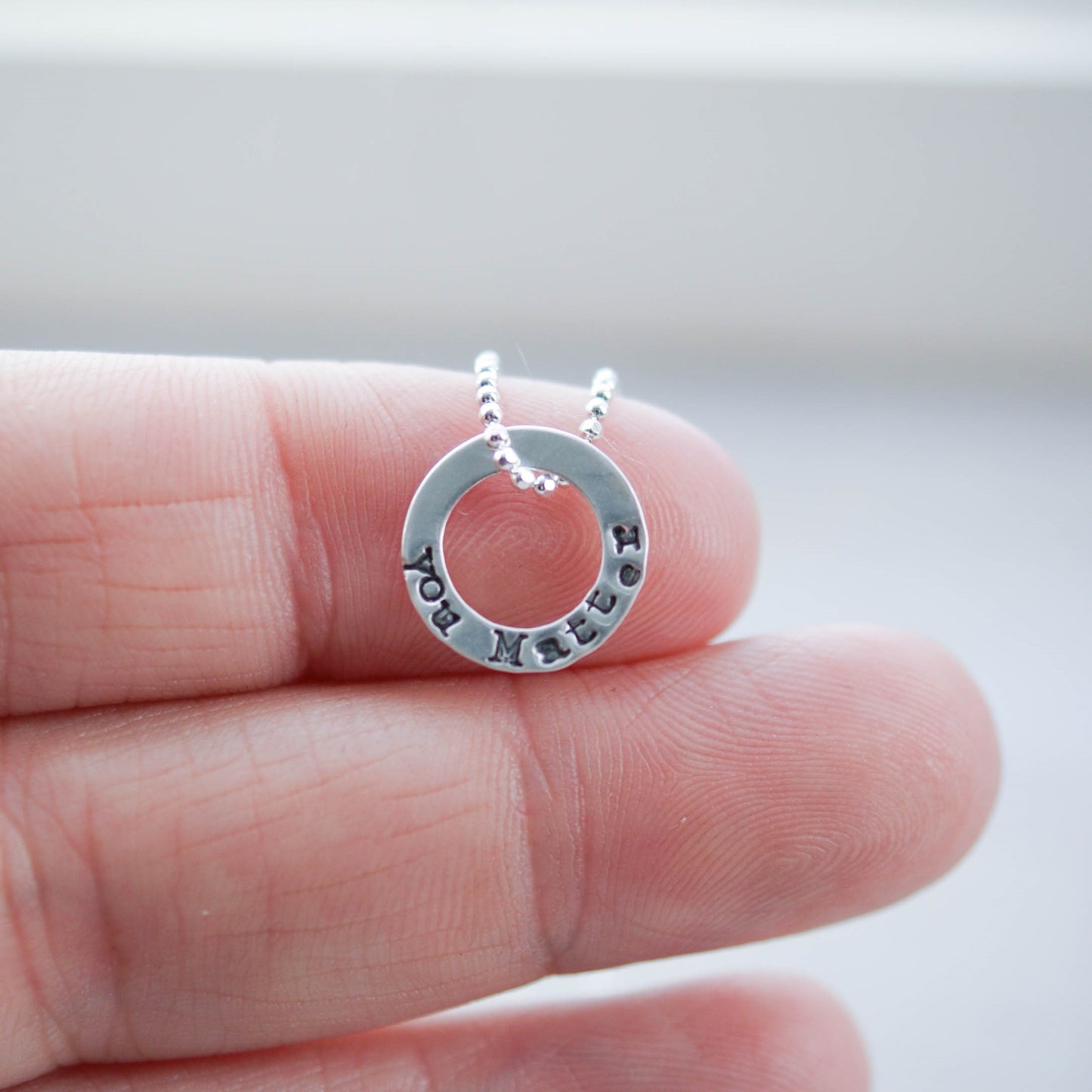 Tiny circle necklace in sterling silver stamped with You Matter on hand