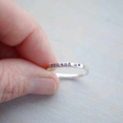 Skinny sterling silver ring stamped with you and me held between fingers