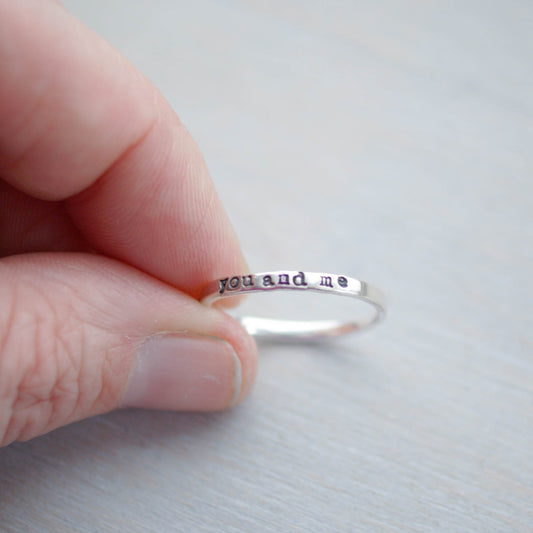 Skinny sterling silver ring stamped with you and me held between fingers