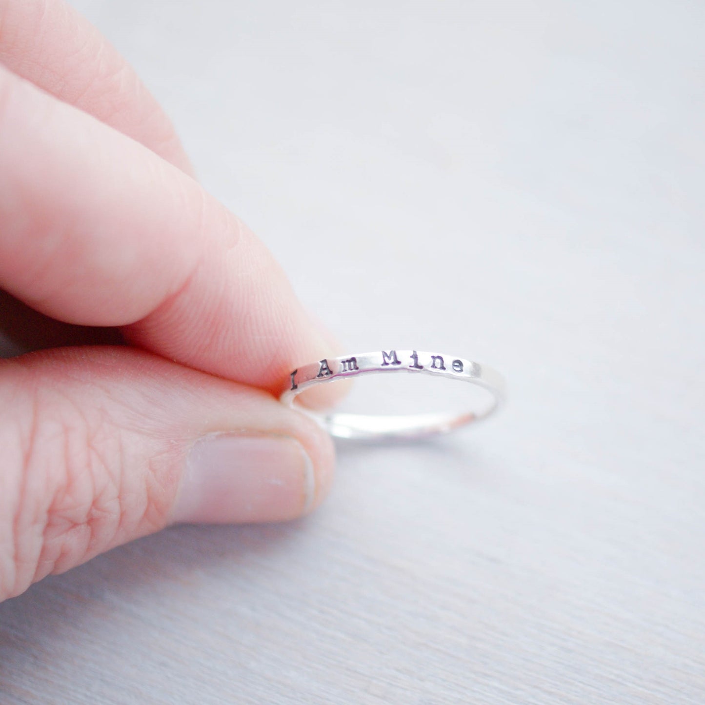 Sterling Silver Stacking Ring handstamped with I Am Mine being held between fingers