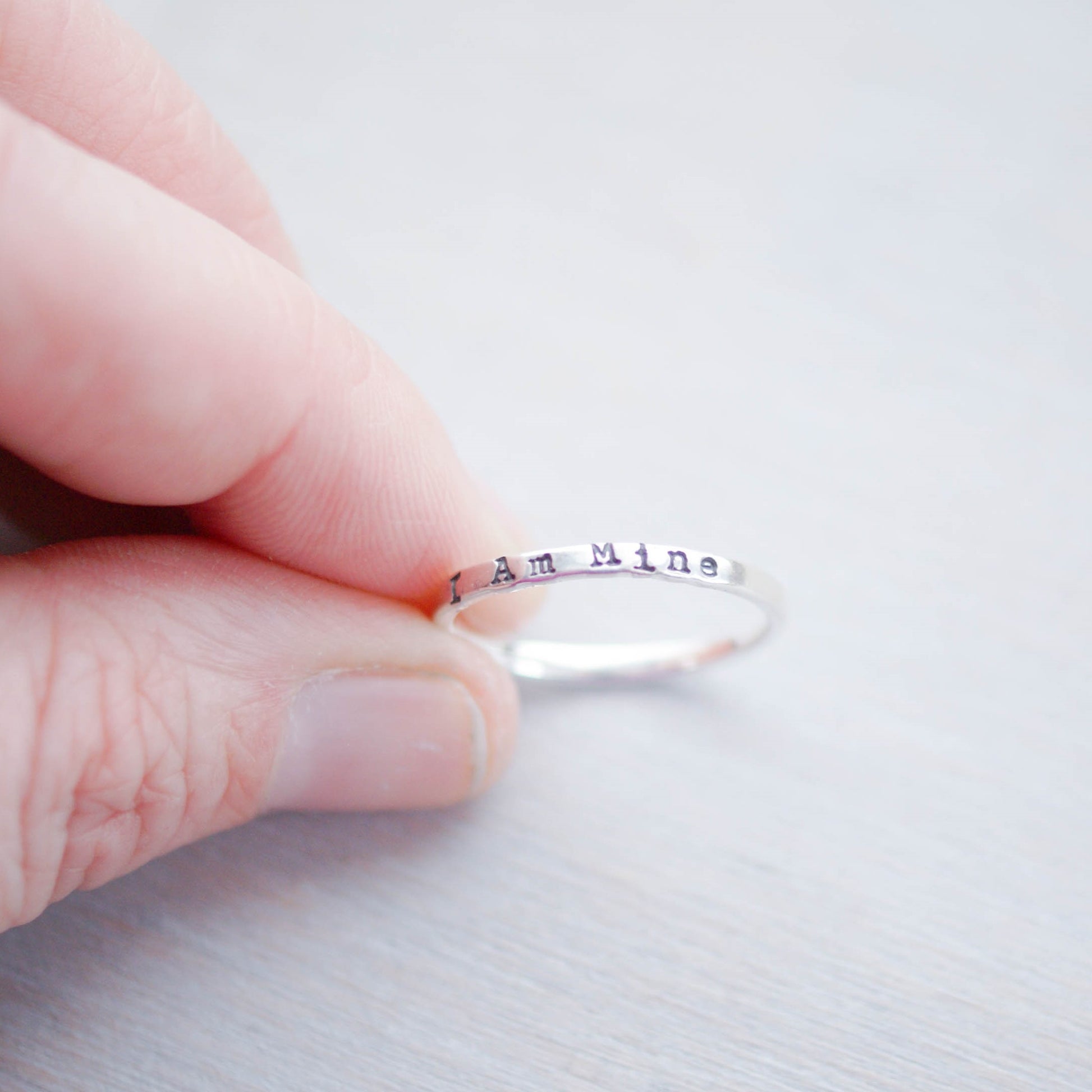 Sterling Silver Stacking Ring handstamped with I Am Mine being held between fingers