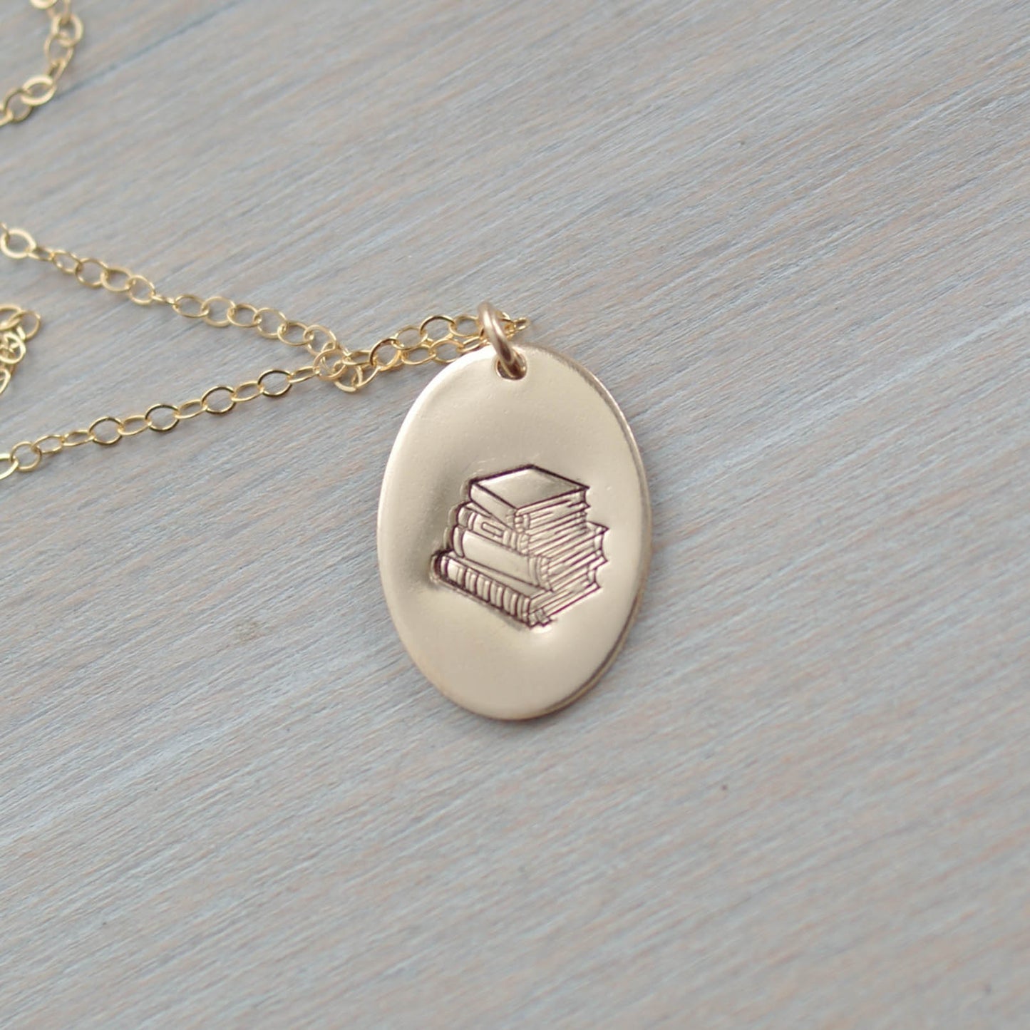 Gold oval necklace stamped with a stack of books