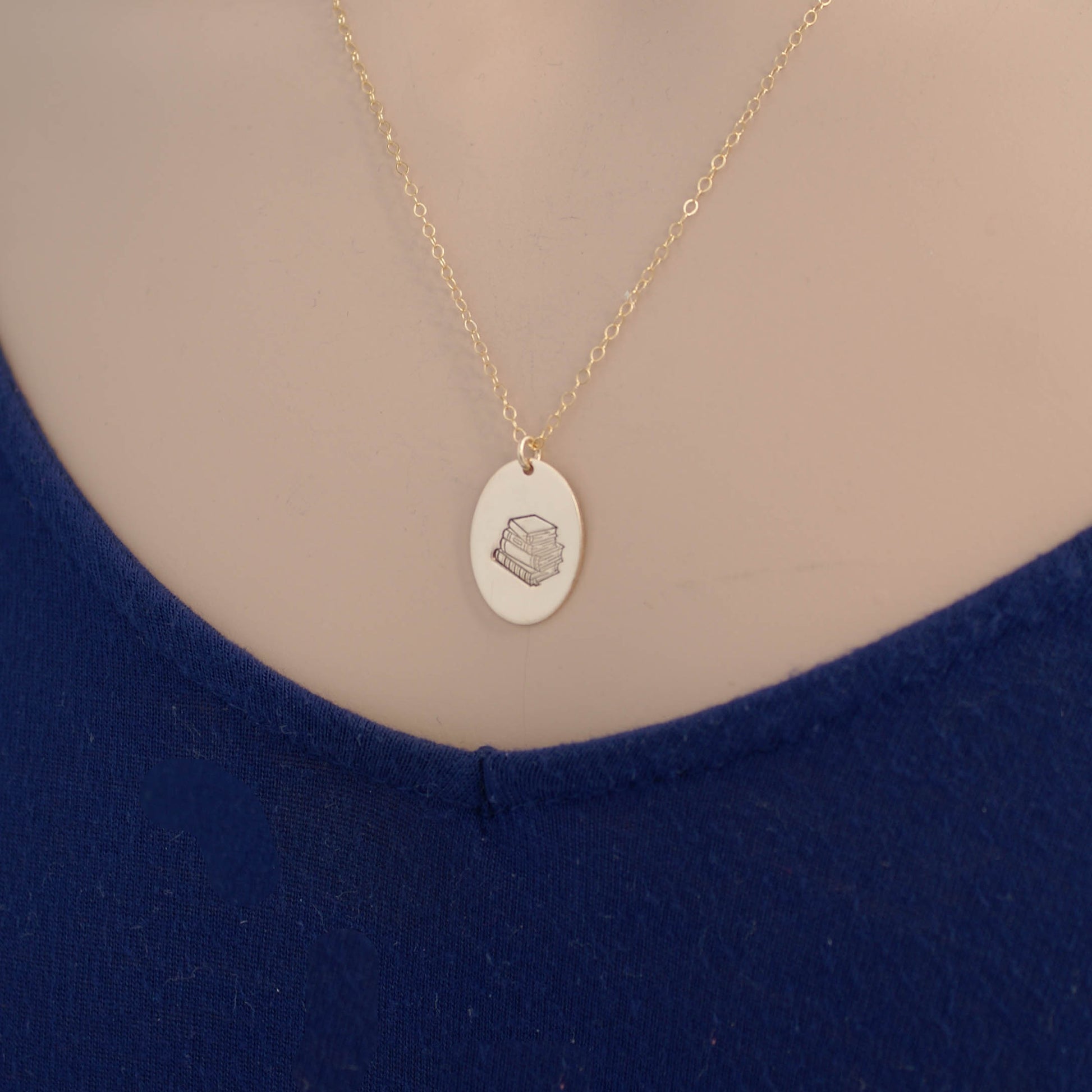 Gold oval necklace stamped with a stack of books on neck