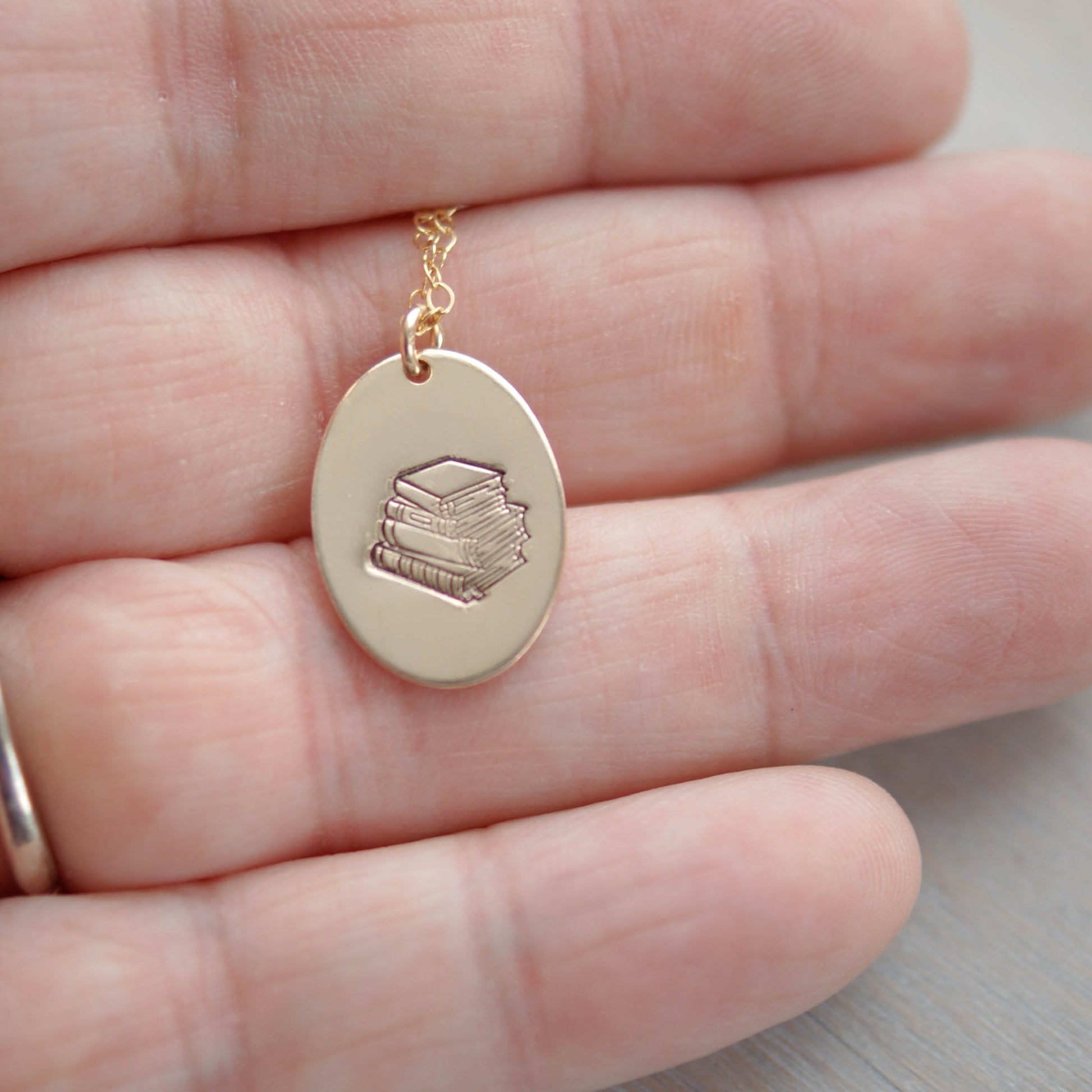 Gold oval necklace stamped with a stack of books in hand