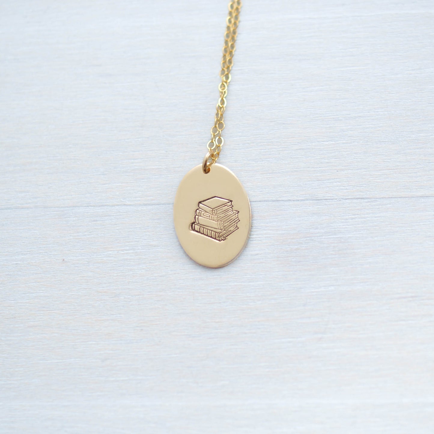 Gold oval necklace stamped with a stack of books