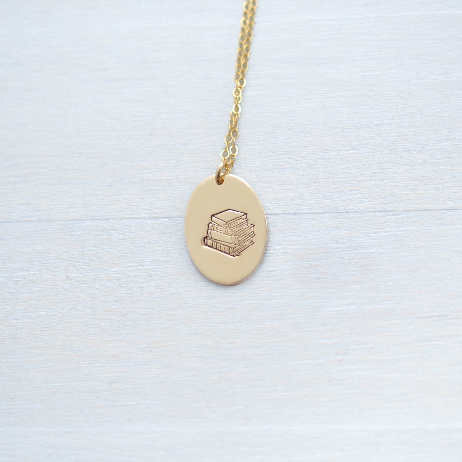 Gold oval necklace stamped with a stack of books