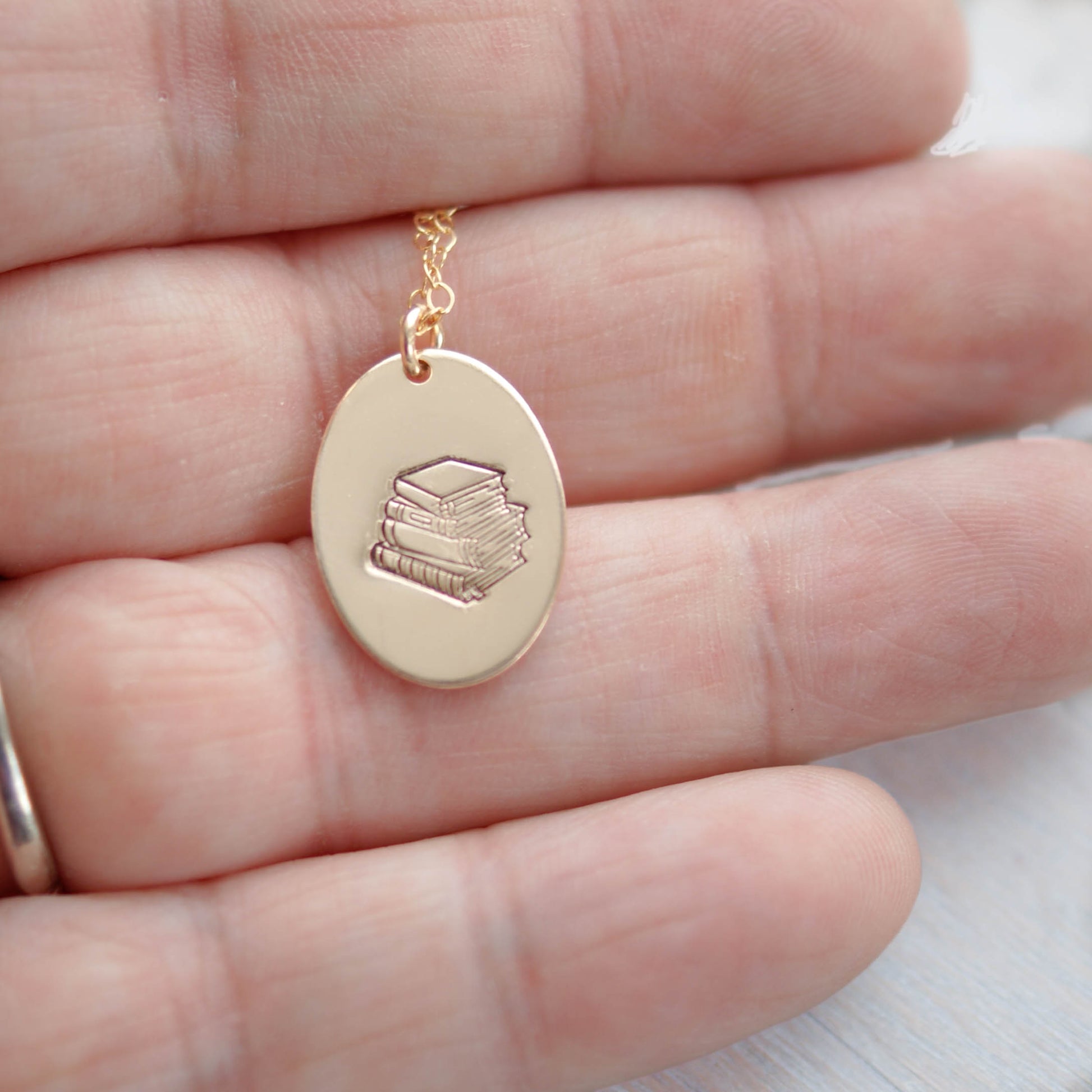 Gold oval necklace stamped with a stack of books in hand