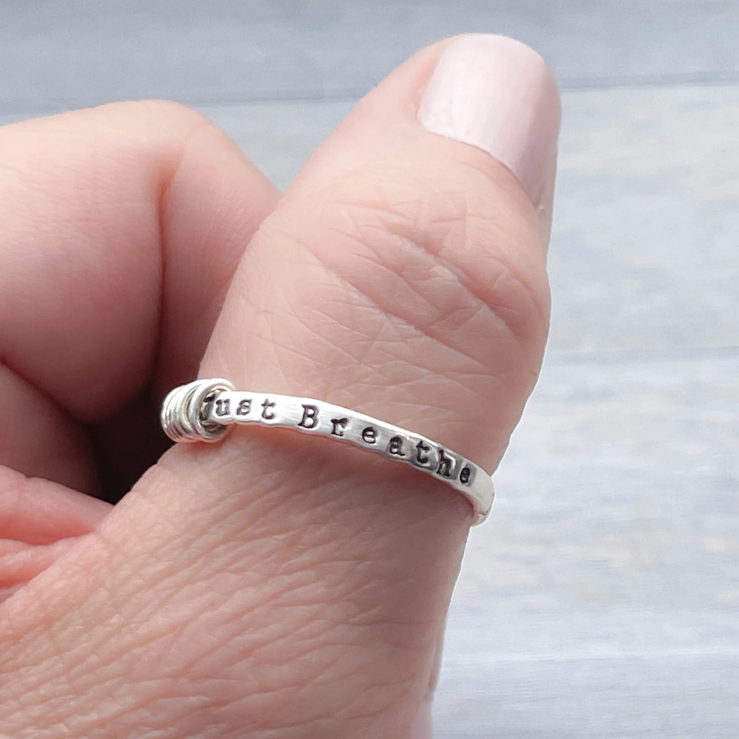 image of sterling silver ring stamped with Just Breathe on a hand