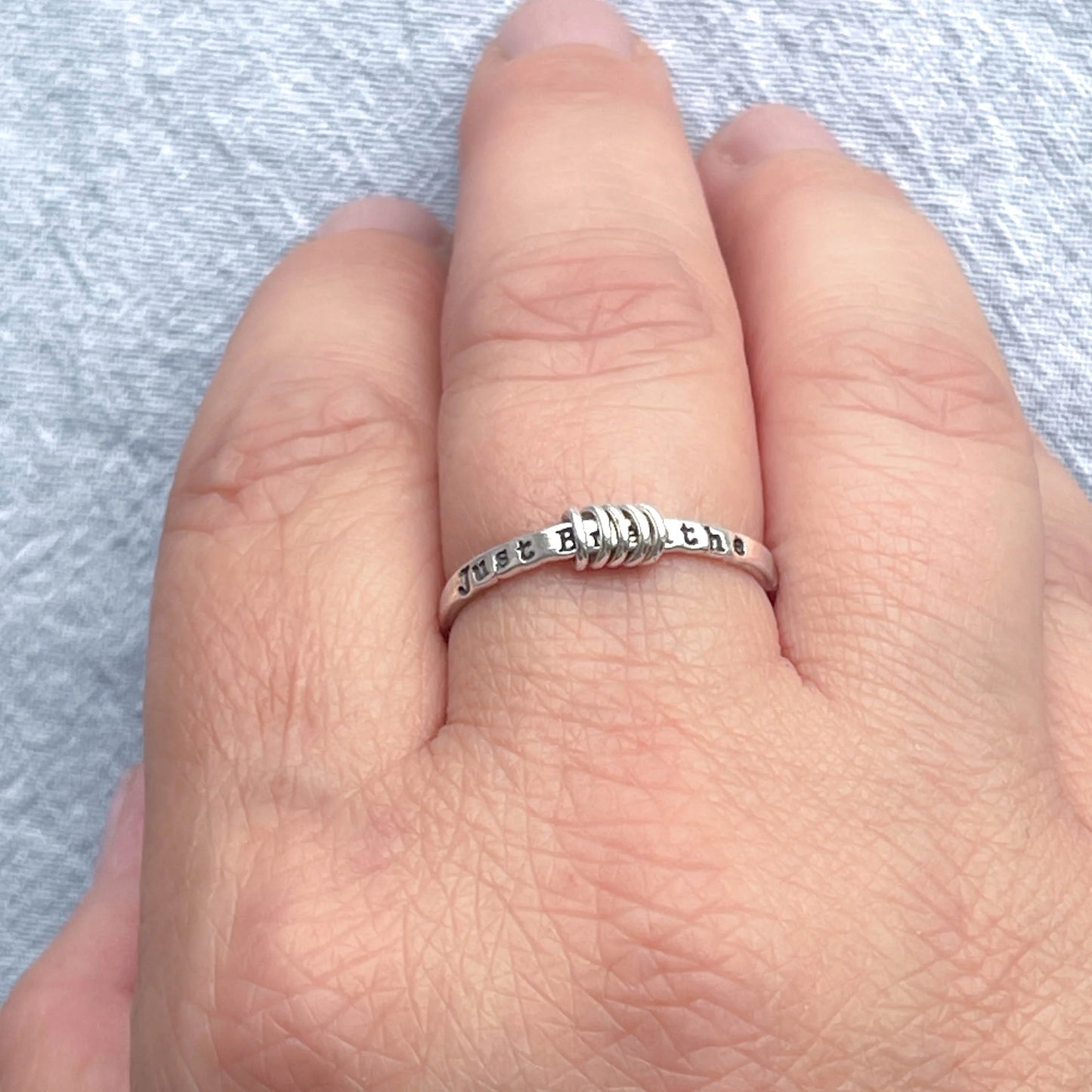 image of sterling silver ring stamped with Just Breathe on a hand