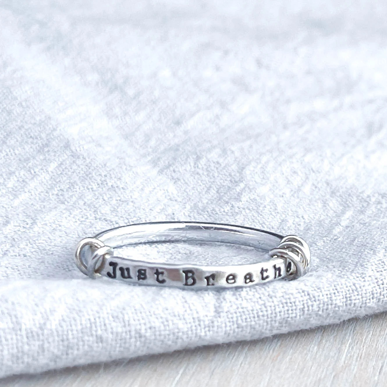 image of sterling silver ring stamped with Just Breathe on a blue fabric