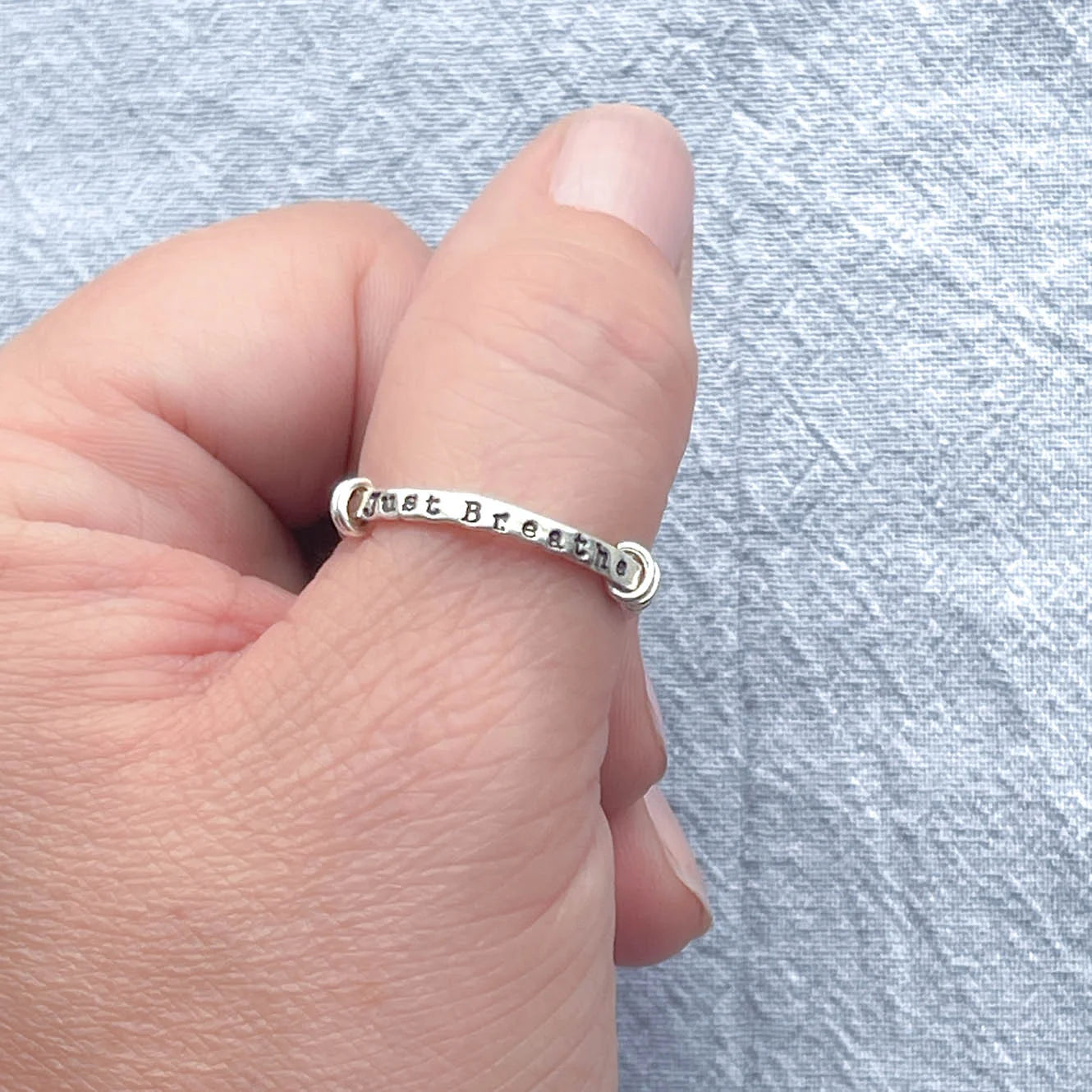 image of sterling silver ring stamped with Just Breathe on a hand