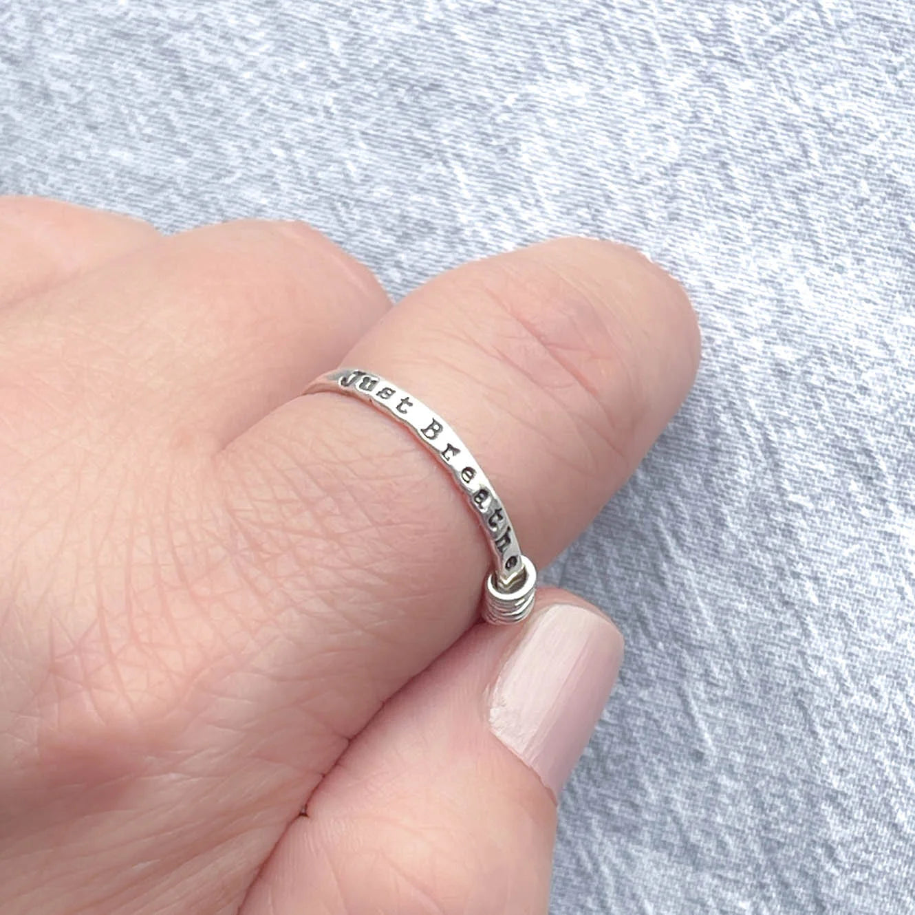 image of sterling silver ring stamped with Just Breathe on a hand