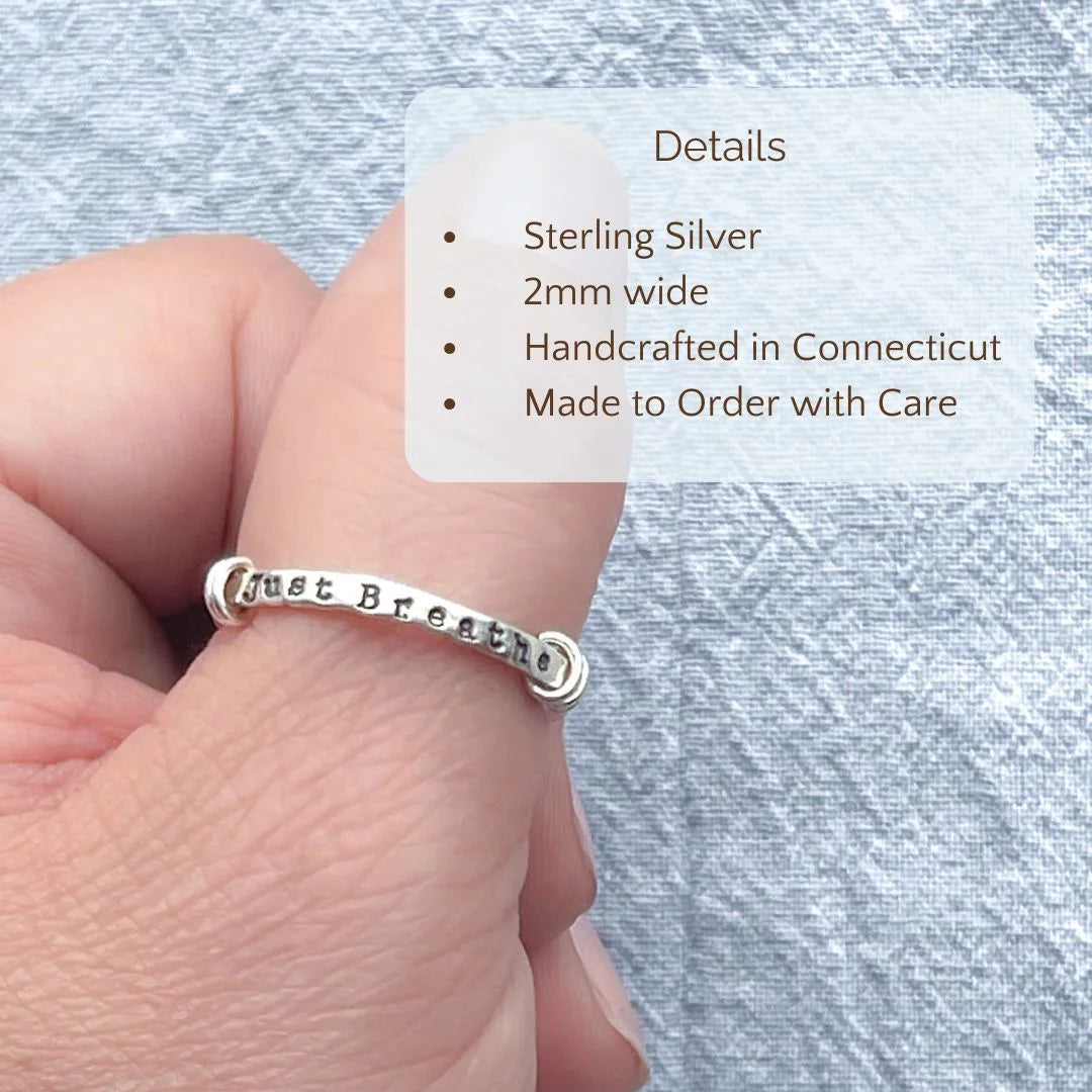image of sterling silver just breathe anxiety spinner ring on thumb over a grey background