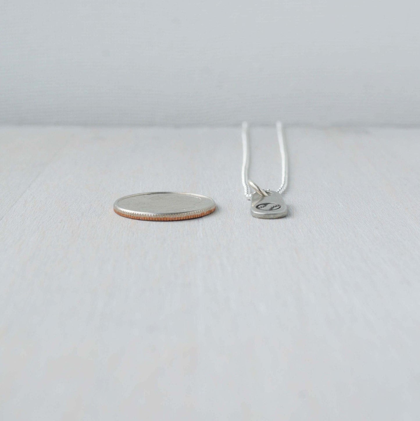 Silver baseball necklace in artisan pewter next to dime