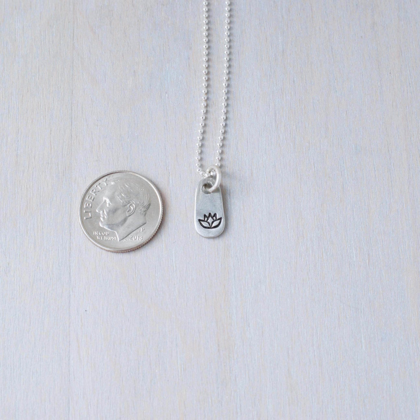 Silver lotus necklace in artisan pewter next to dime