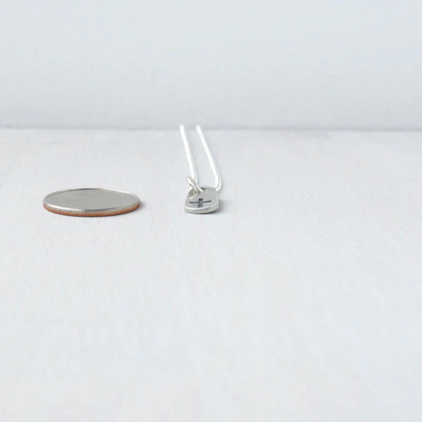 image of tiny cross necklace next to dime