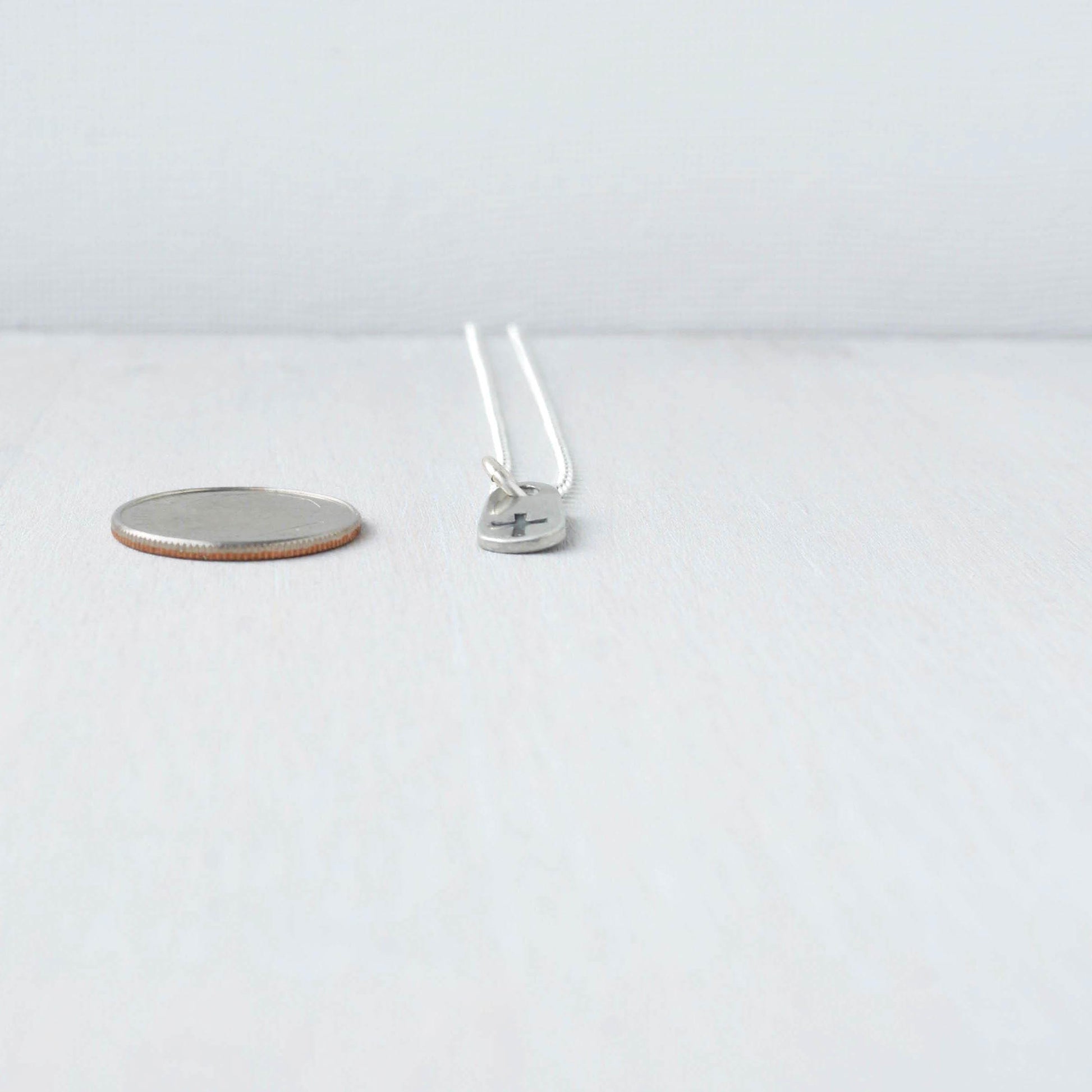 image of tiny cross necklace next to dime