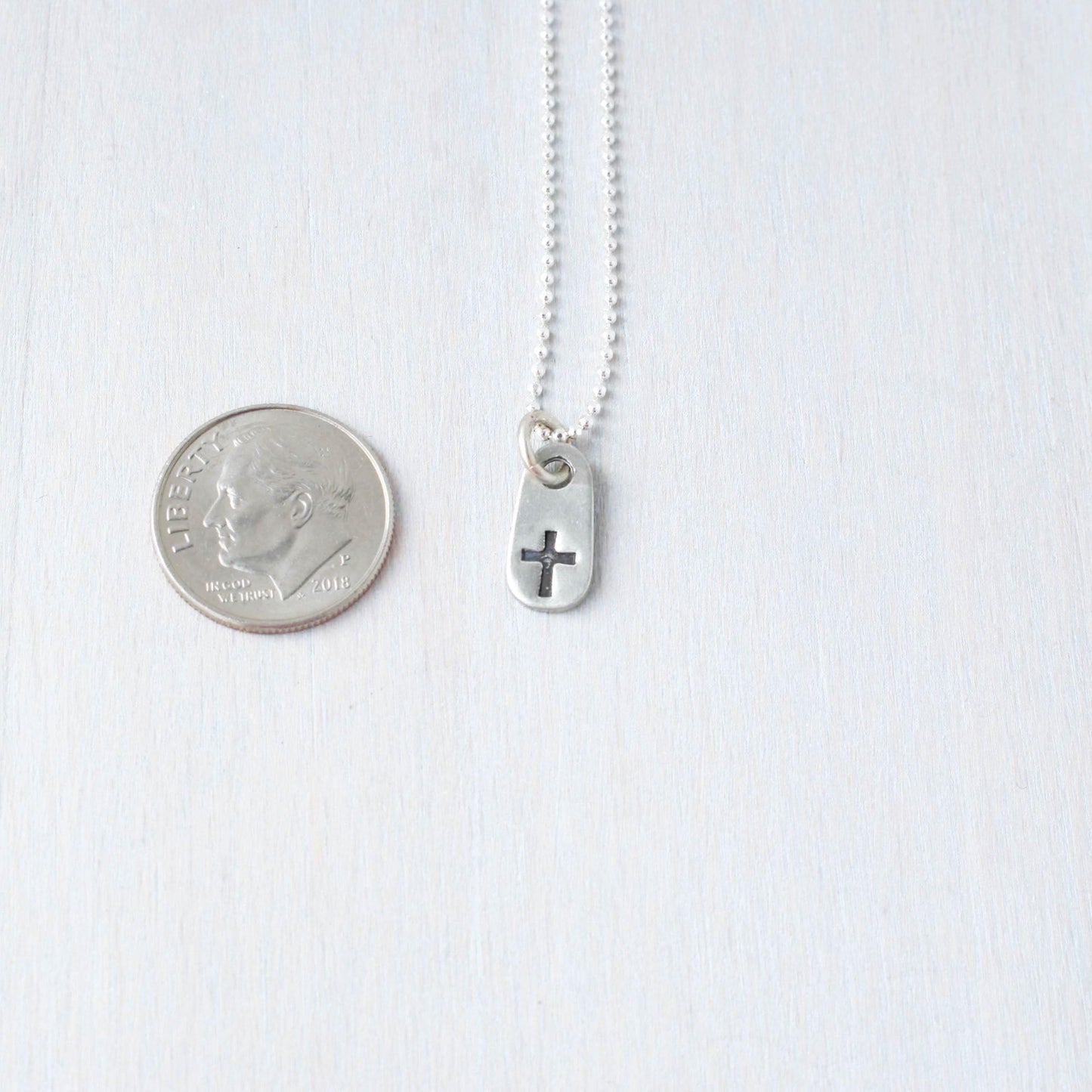 image of small cross necklace next to dime