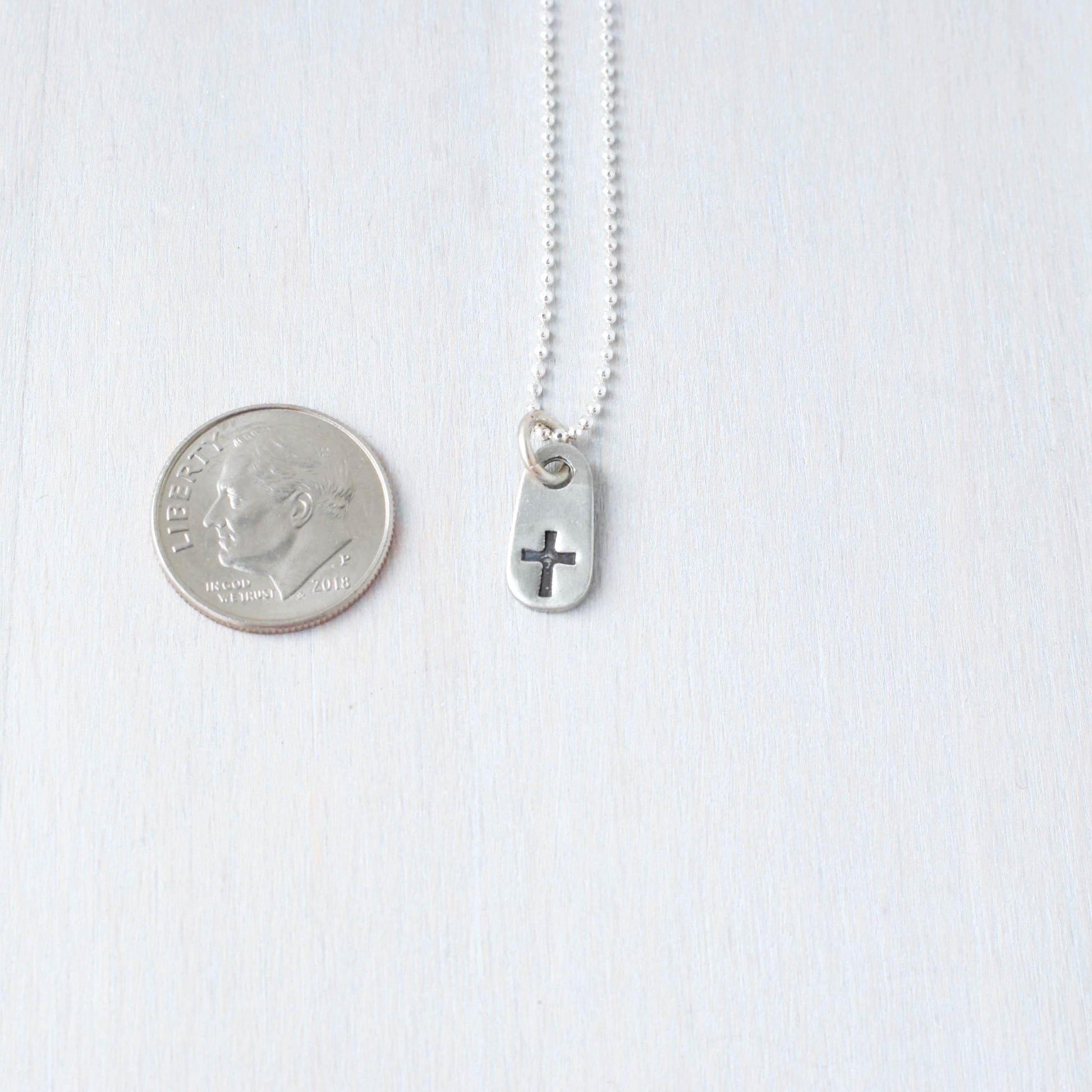 image of small cross necklace next to dime