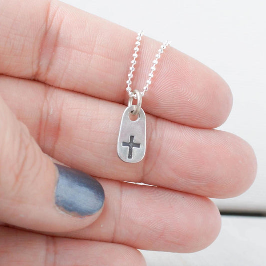 image of tiny cross necklace being held in hand