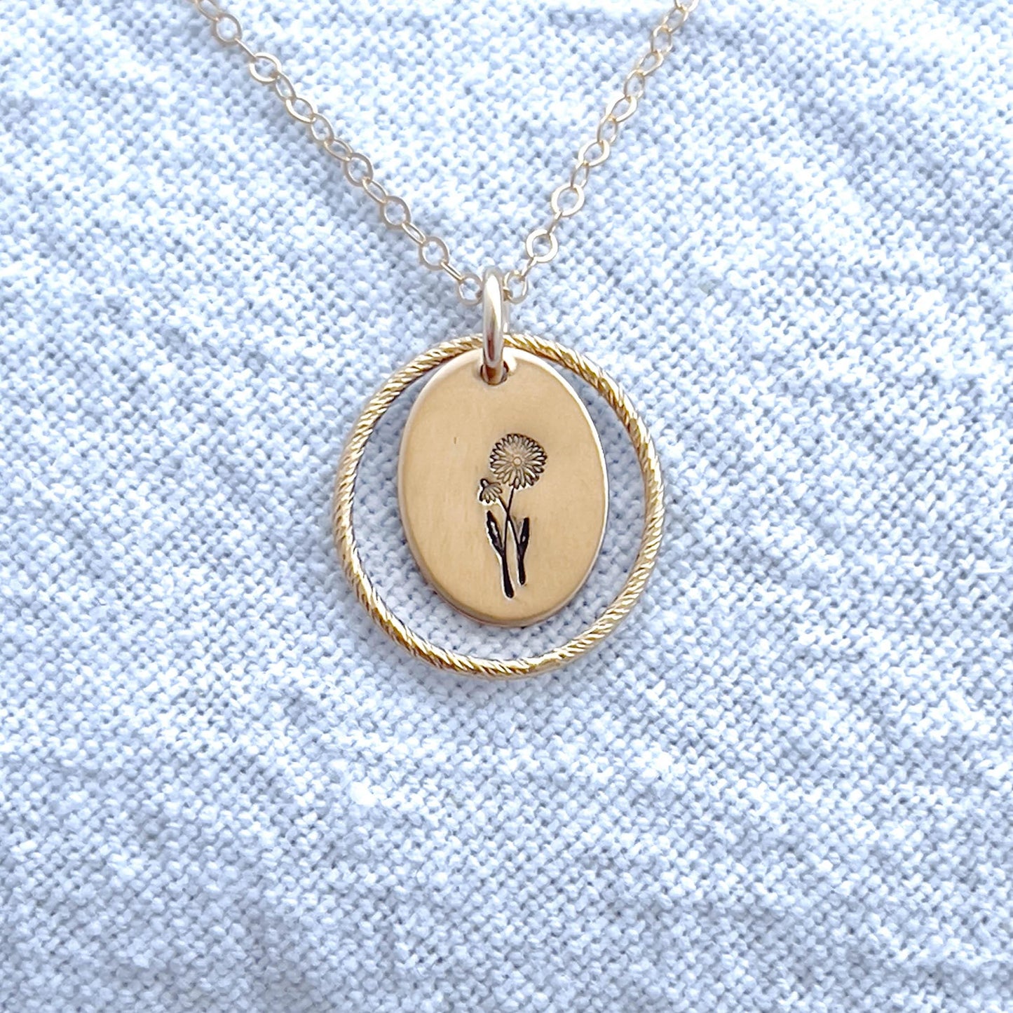 image of a gold oval april birth flower necklace with a daisy stamped on it for april and a sparkle oval link surrounding it.