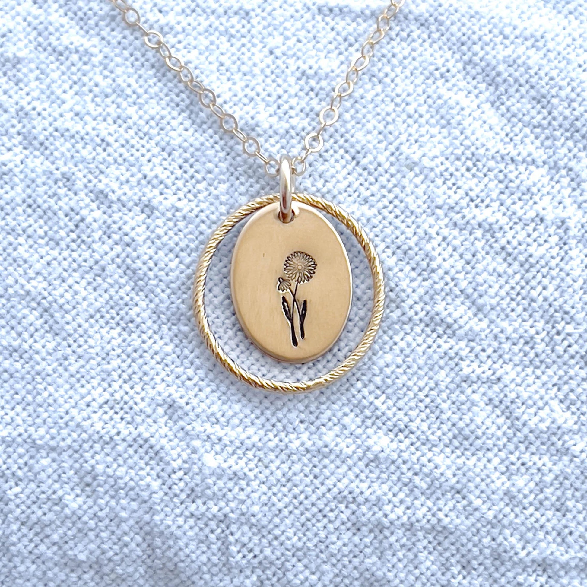 image of a gold oval april birth flower necklace with a daisy stamped on it for april and a sparkle oval link surrounding it.