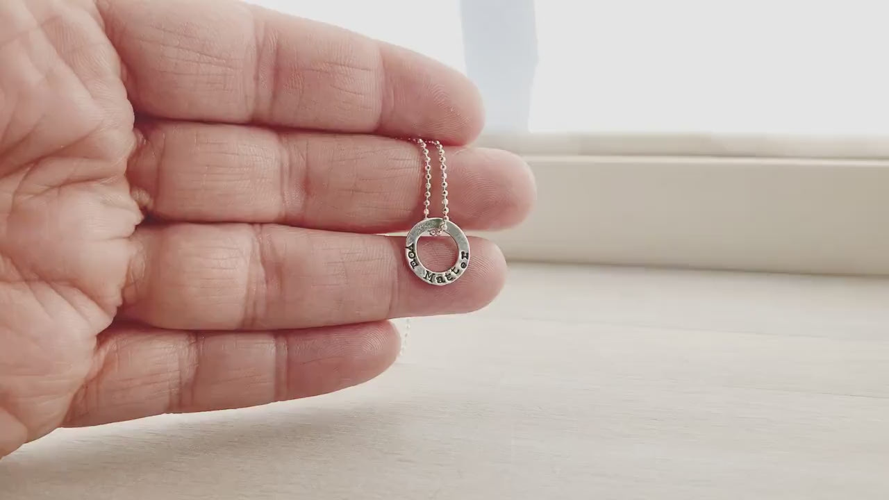 Tiny circle necklace in sterling silver stamped with You Matter on hand and on neck