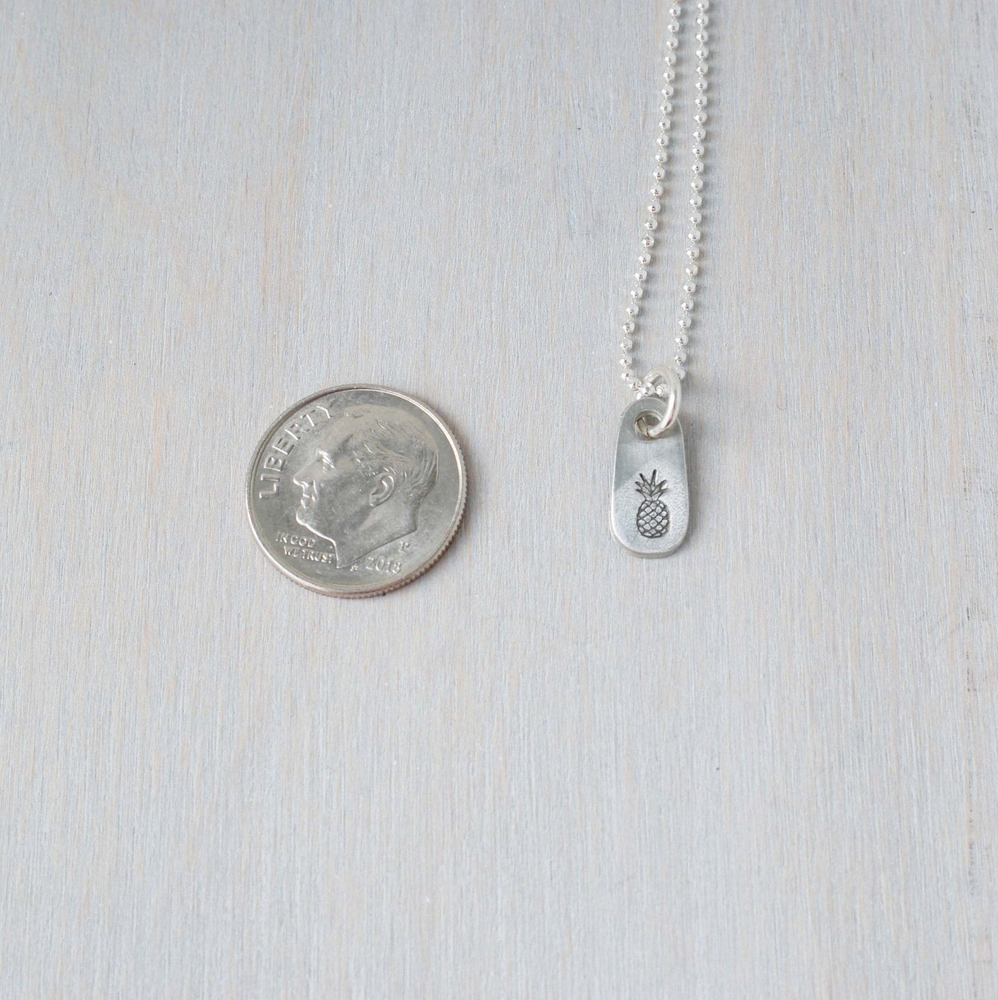 Dainty silver Pineapple necklace in artisan pewter next to a dime