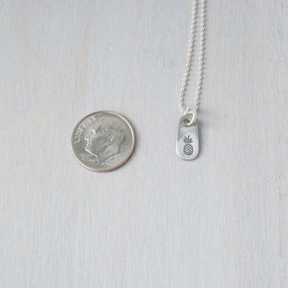 Dainty silver Pineapple necklace in artisan pewter next to a dime
