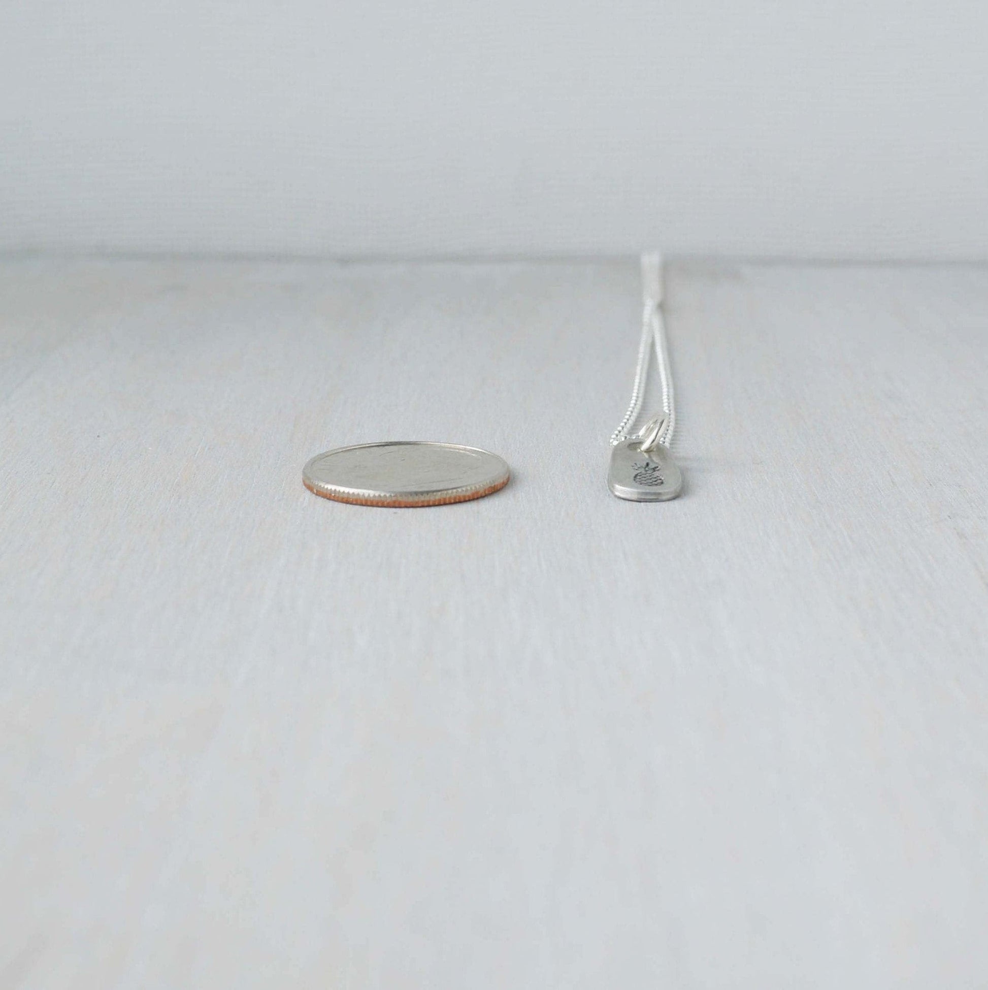 Dainty silver Pineapple necklace in artisan pewter next to a dime