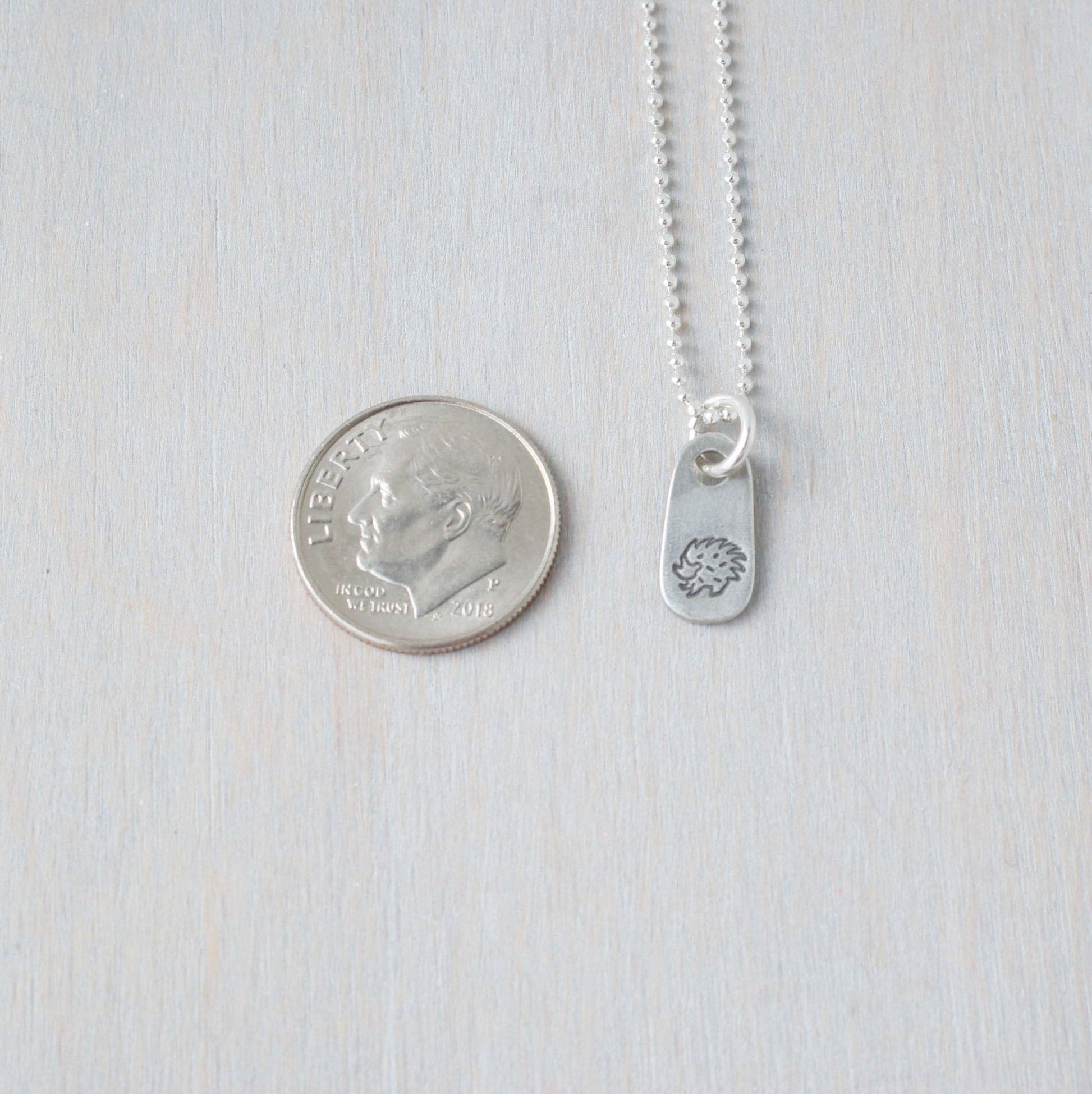 Silver hedgehog necklace in artisan pewter next to dime