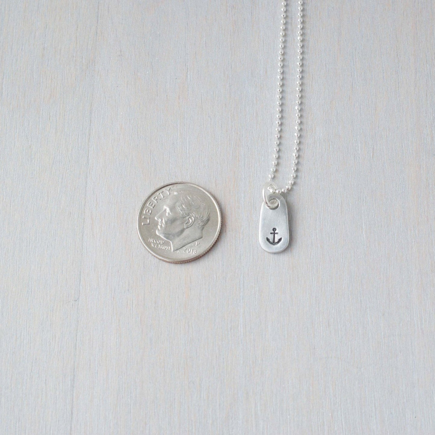 Dainty Handstamped Anchor Necklace in Pewter next to dime for scale