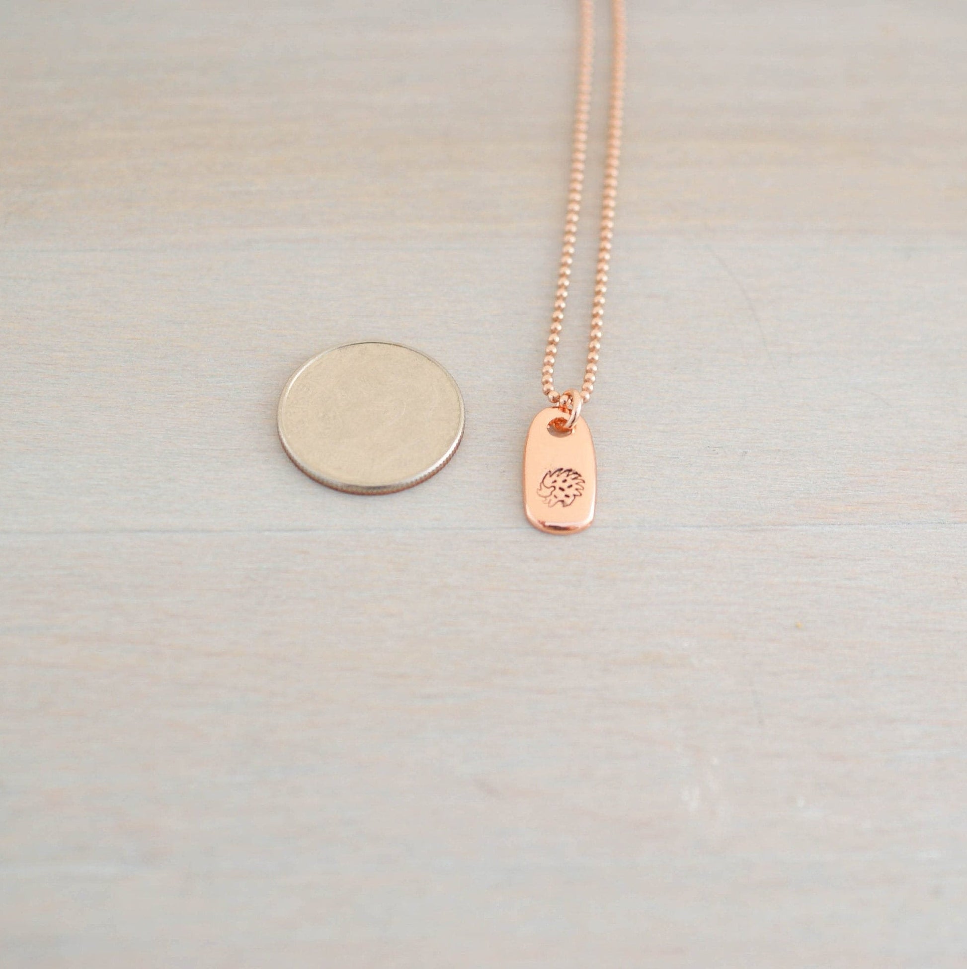 Rose gold hedgehog necklace next to dime
