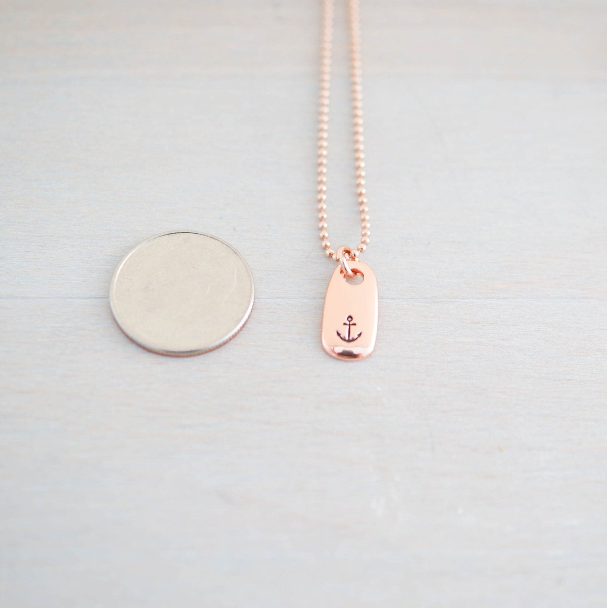 Refuse to Sink Anchor Necklace in Rose Gold next to dime for scale