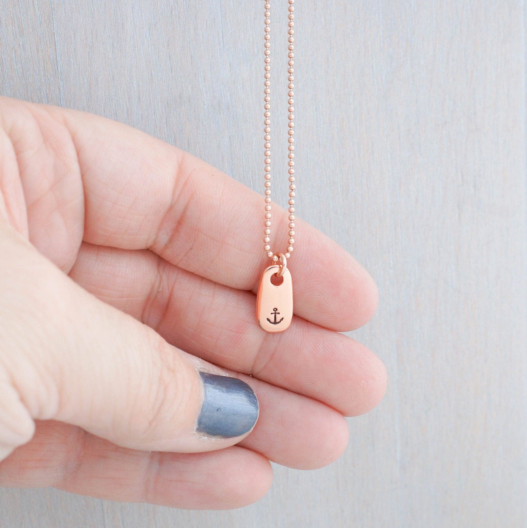 Refuse to Sink Anchor Necklace in Rose Gold held in hand
