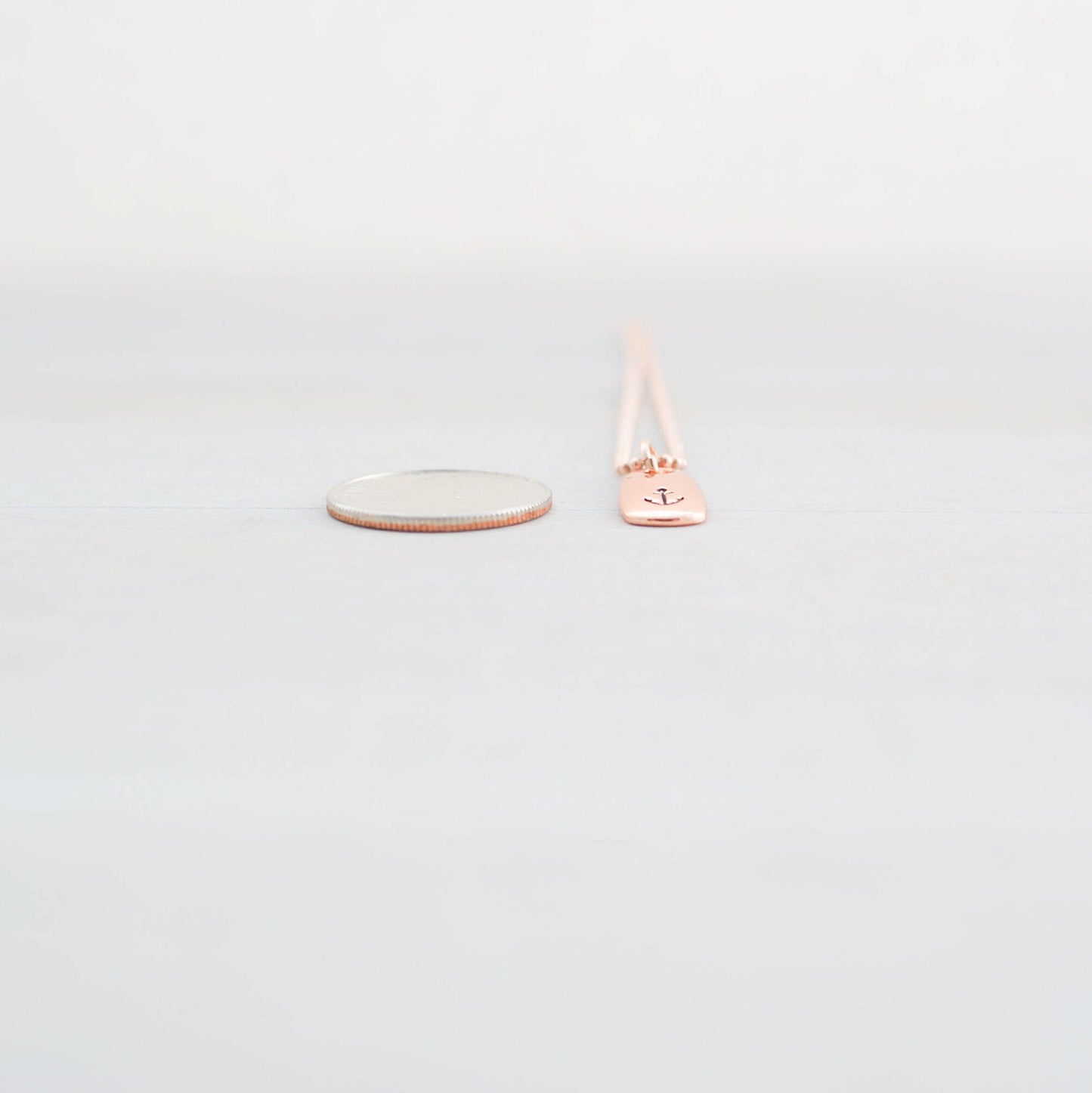 Refuse to Sink Anchor Necklace in Rose Gold next to dime for scale