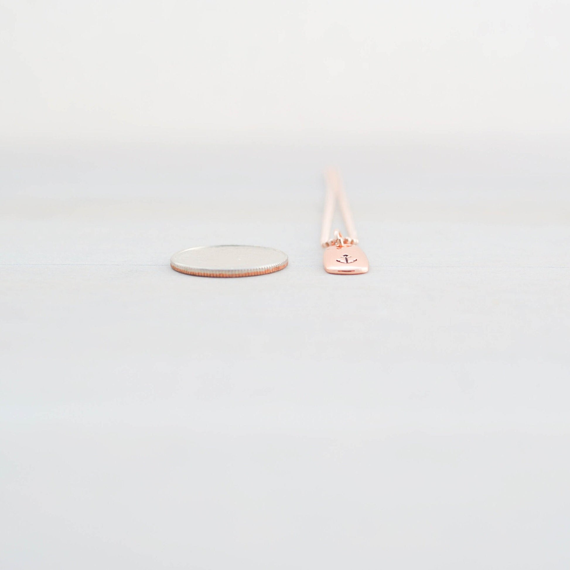 Refuse to Sink Anchor Necklace in Rose Gold next to dime for scale