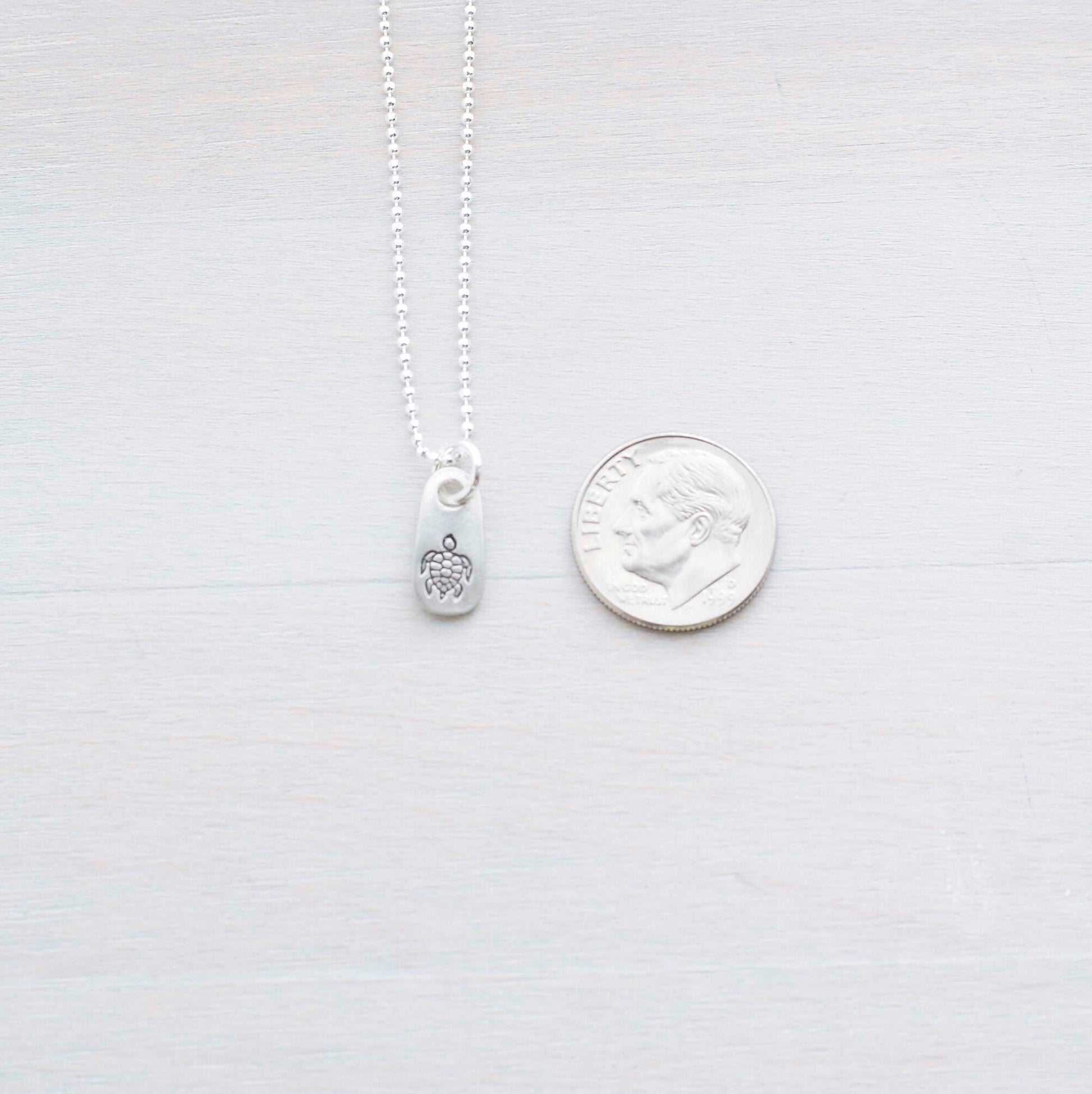 Silver sea turtle necklace in artisan pewter next to a dime