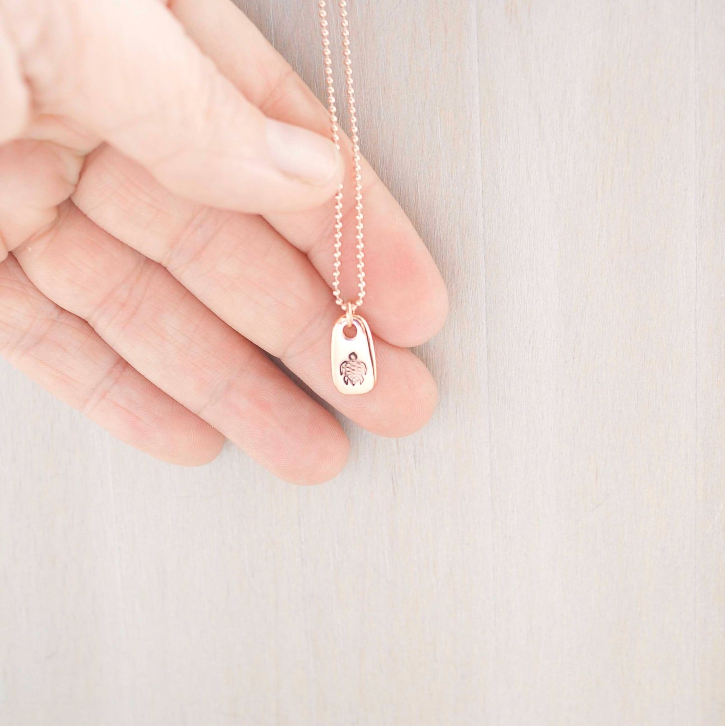 Rose gold necklace stamped with a turtle in hand