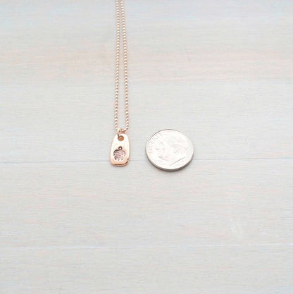 Rose gold necklace stamped with a turtle next to a dime