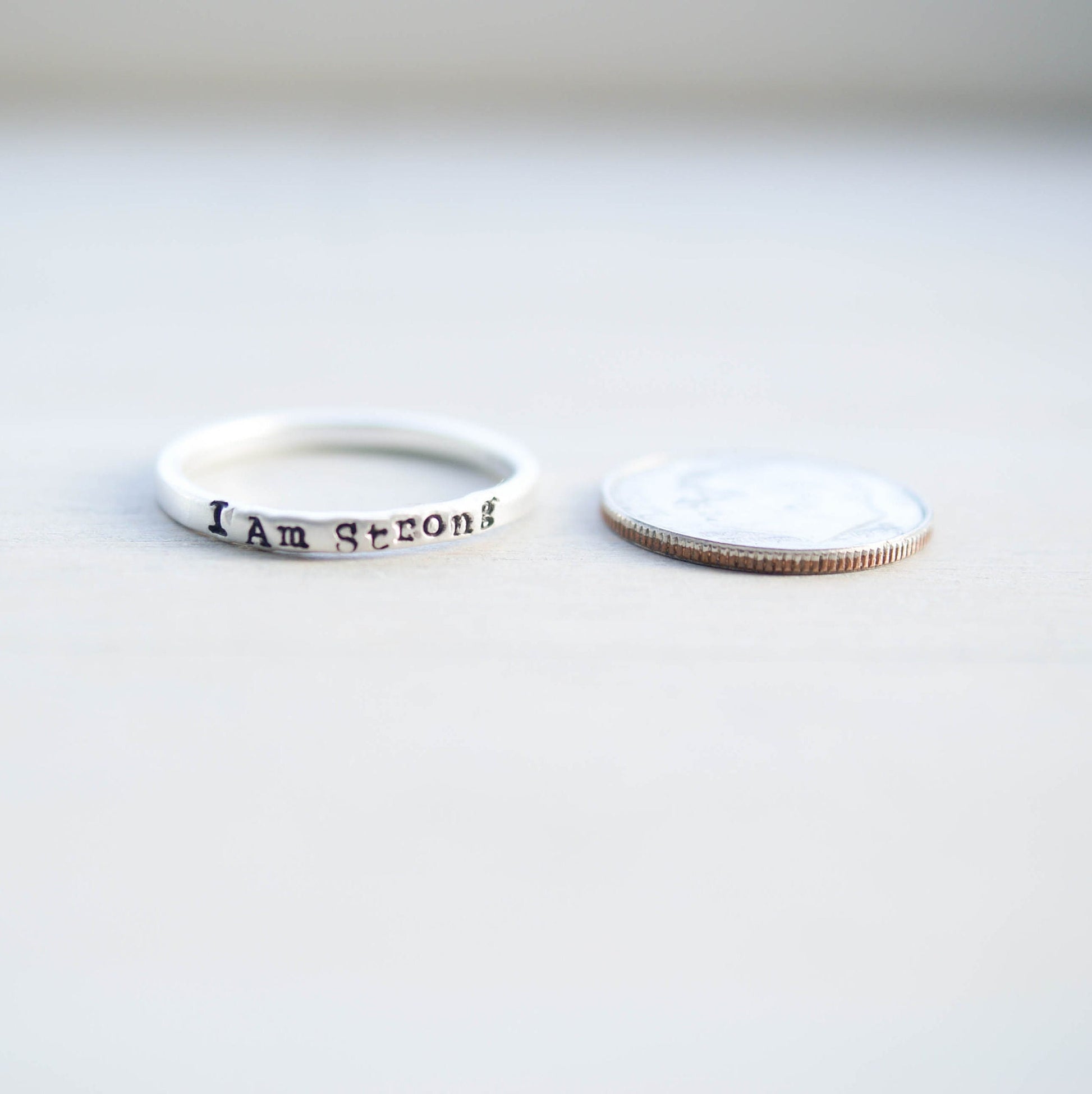 Sterling Silver stacking ring handstmaped with I Am Strong next to dime