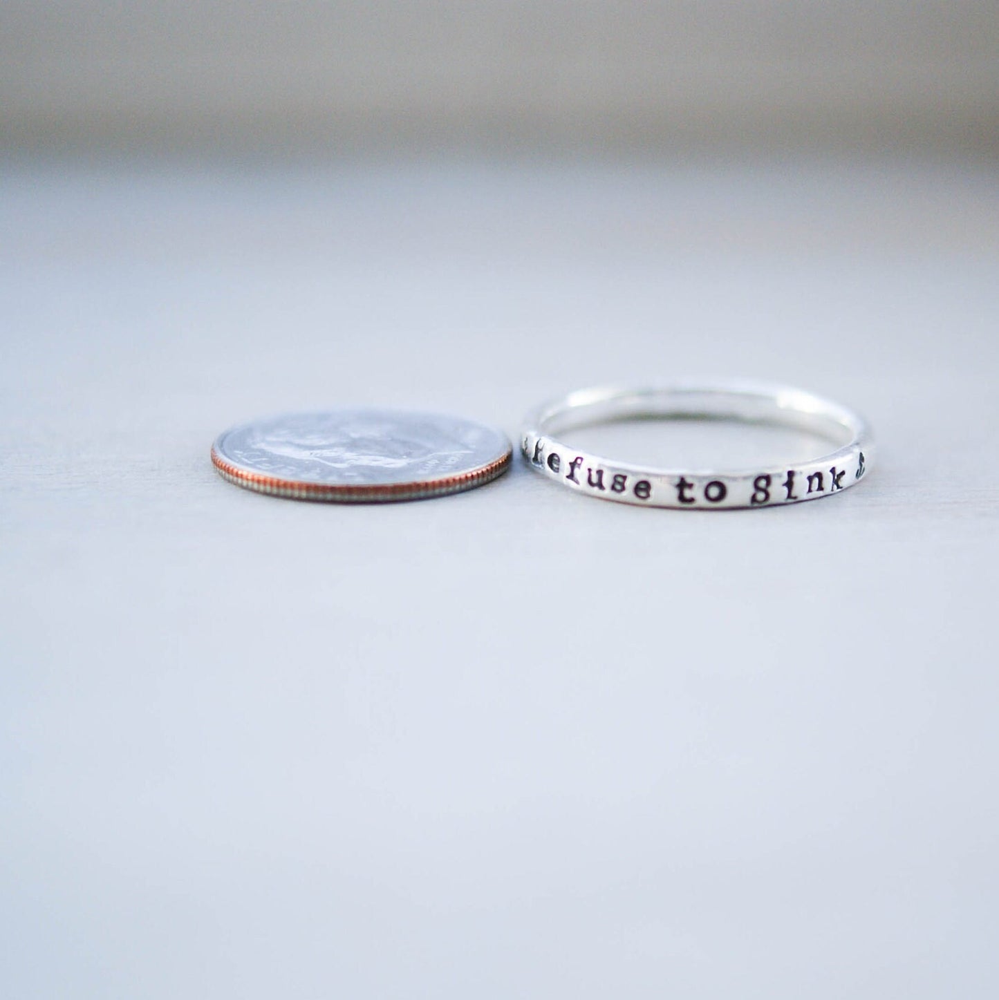 Sterling silver ring handstamped with Refuse to sink next to dime