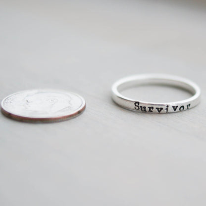 Sterling silver ring stamped with Survivor next to a dime