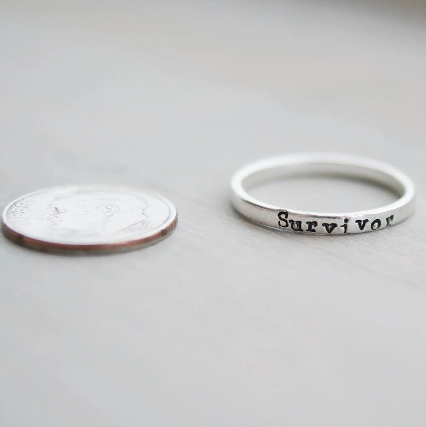 Sterling silver ring stamped with Survivor next to a dime
