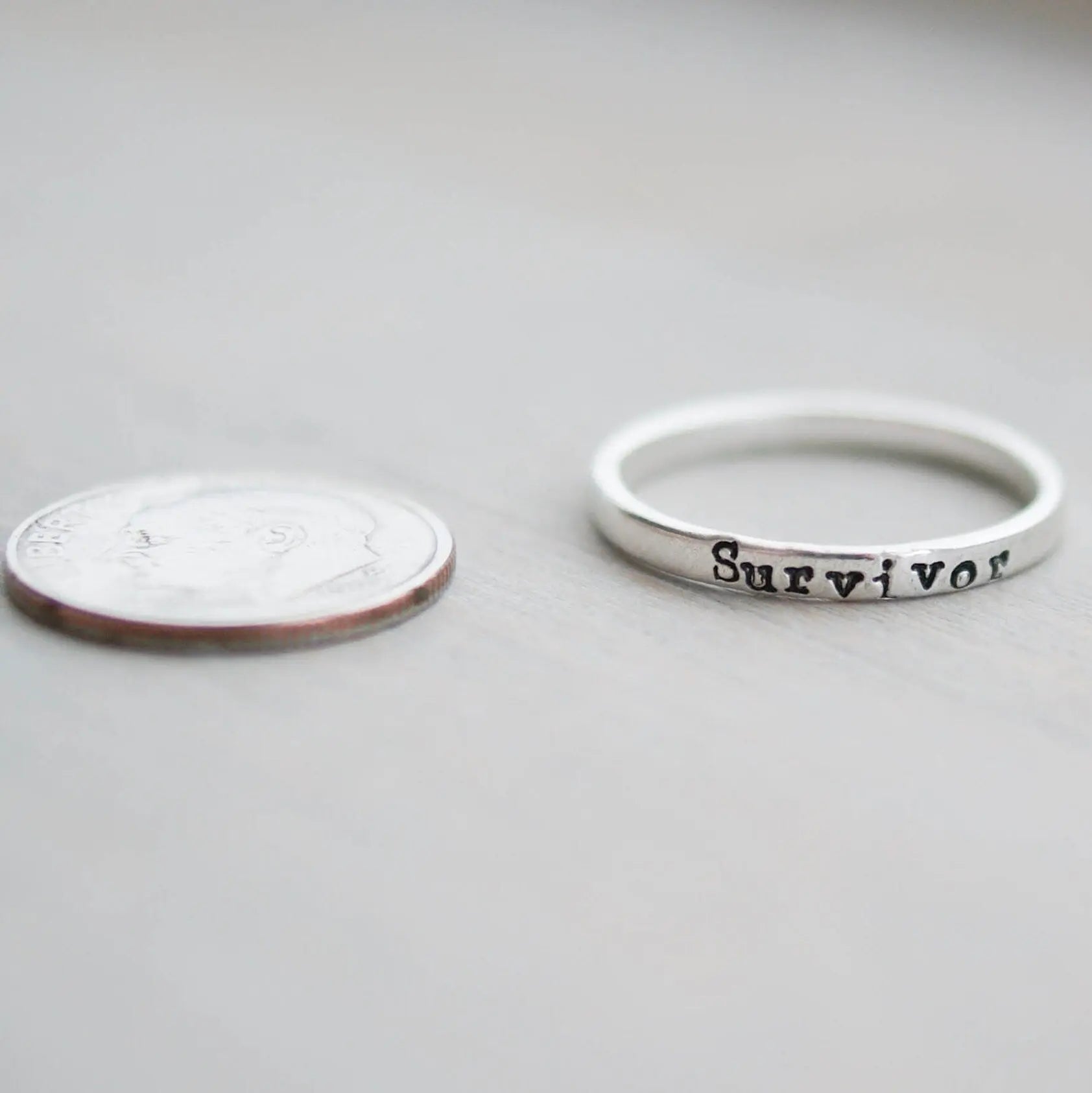 Sterling silver ring stamped with Survivor next to a dime