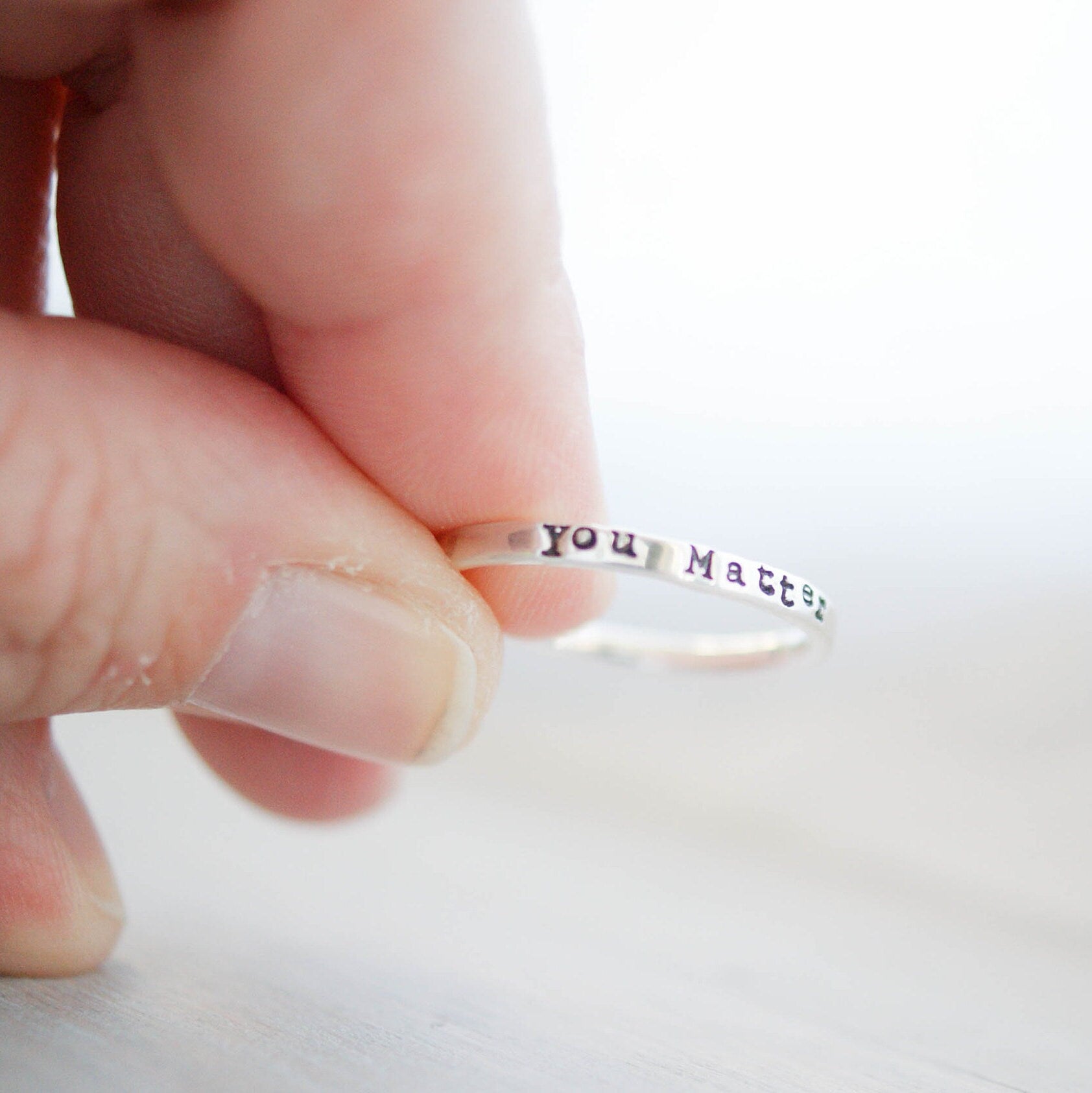 Sterling silver ring stamped with you matter held between fingers