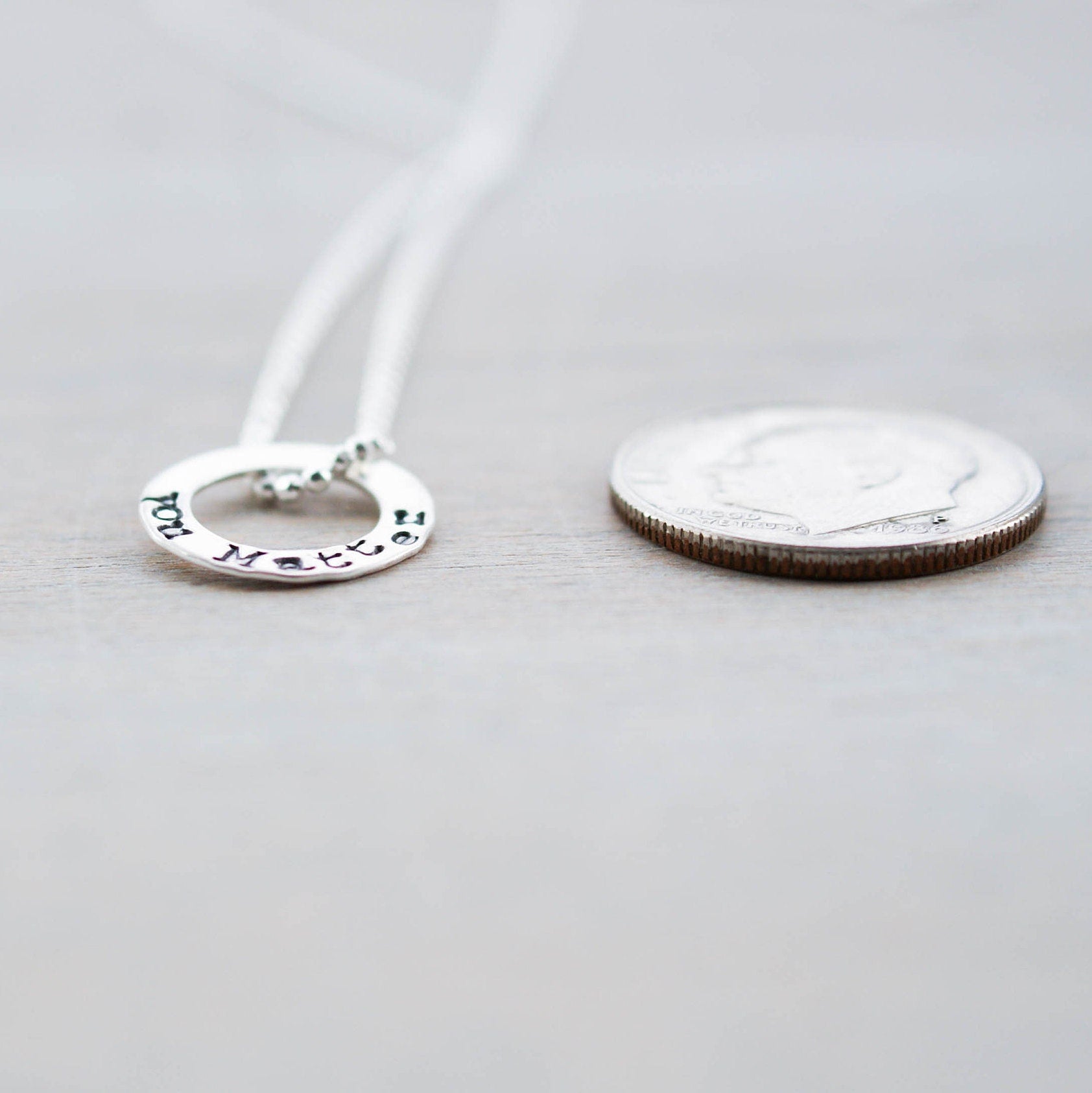 Tiny circle necklace in sterling silver stamped with You Matter next to a dime