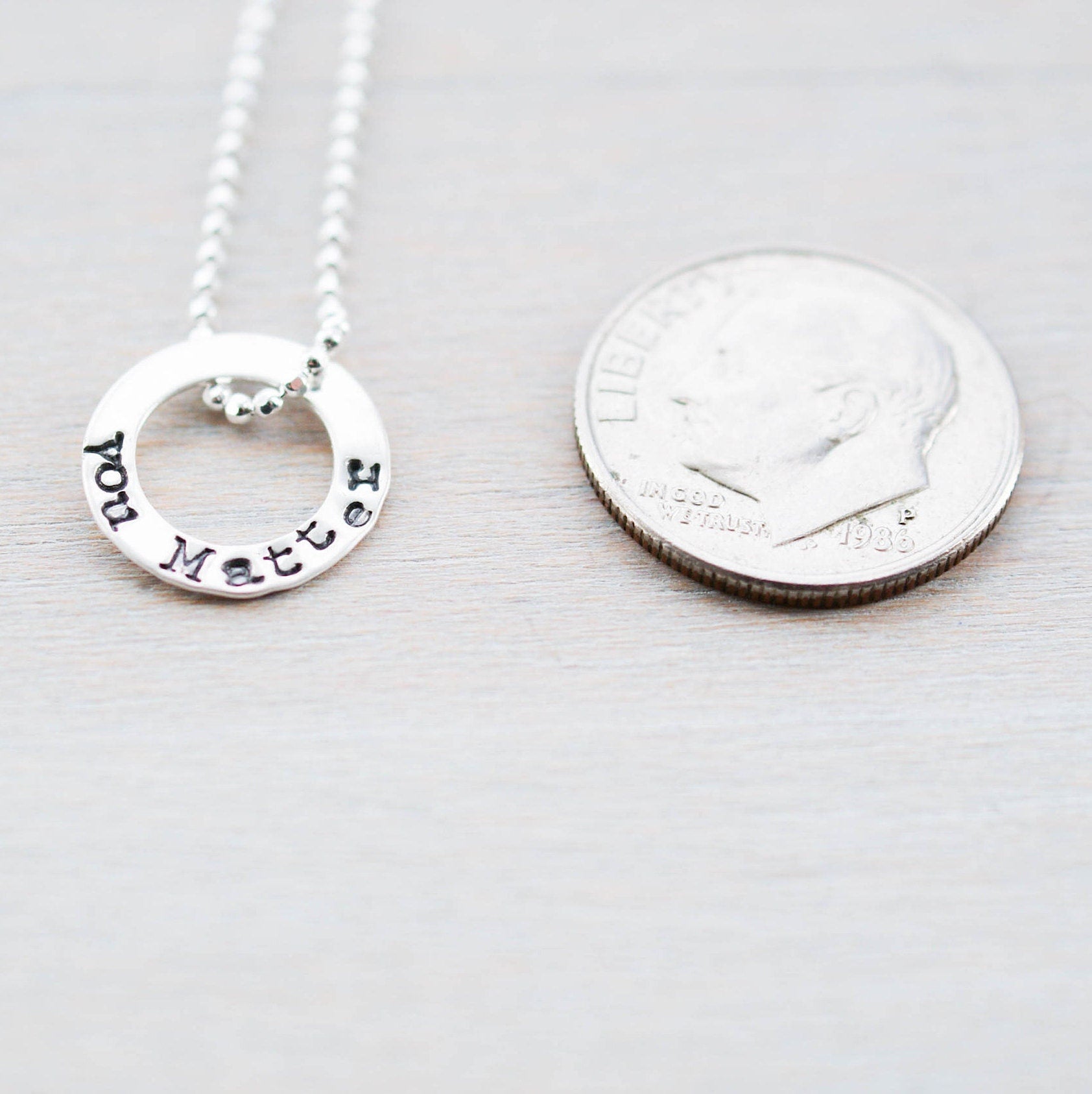 Tiny circle necklace in sterling silver stamped with You Matter next to a dime